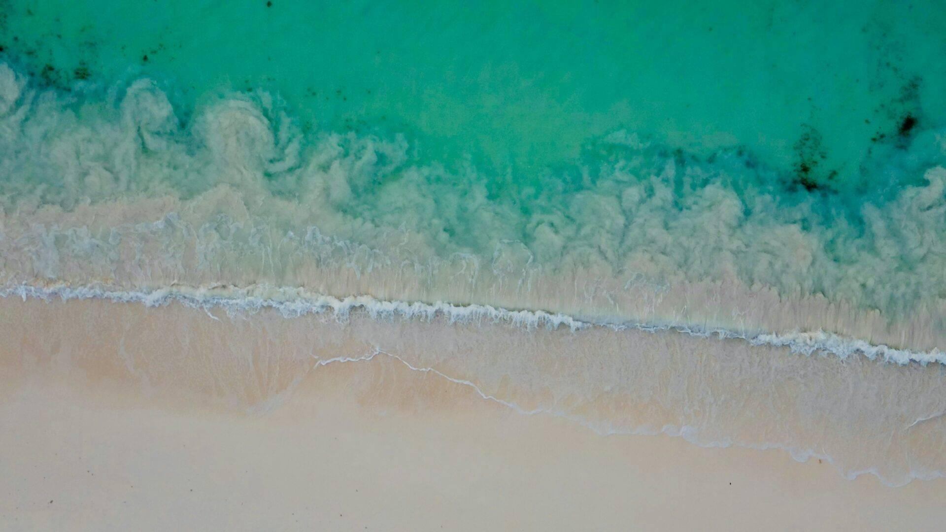 Vista aérea de una playa de arena blanca con olas turquesas y cristalinas rompiendo en la orilla