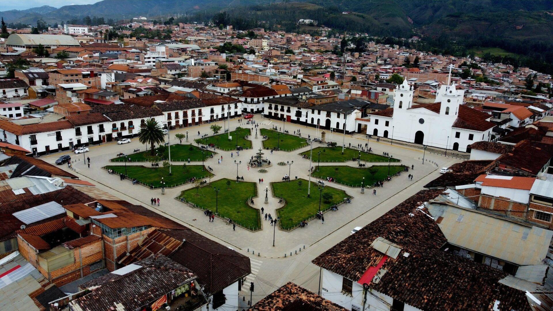 Vista aérea de una gran plaza colonial blanca con iglesia, rodeada de casas de ladrillo rojo en una ciudad andina