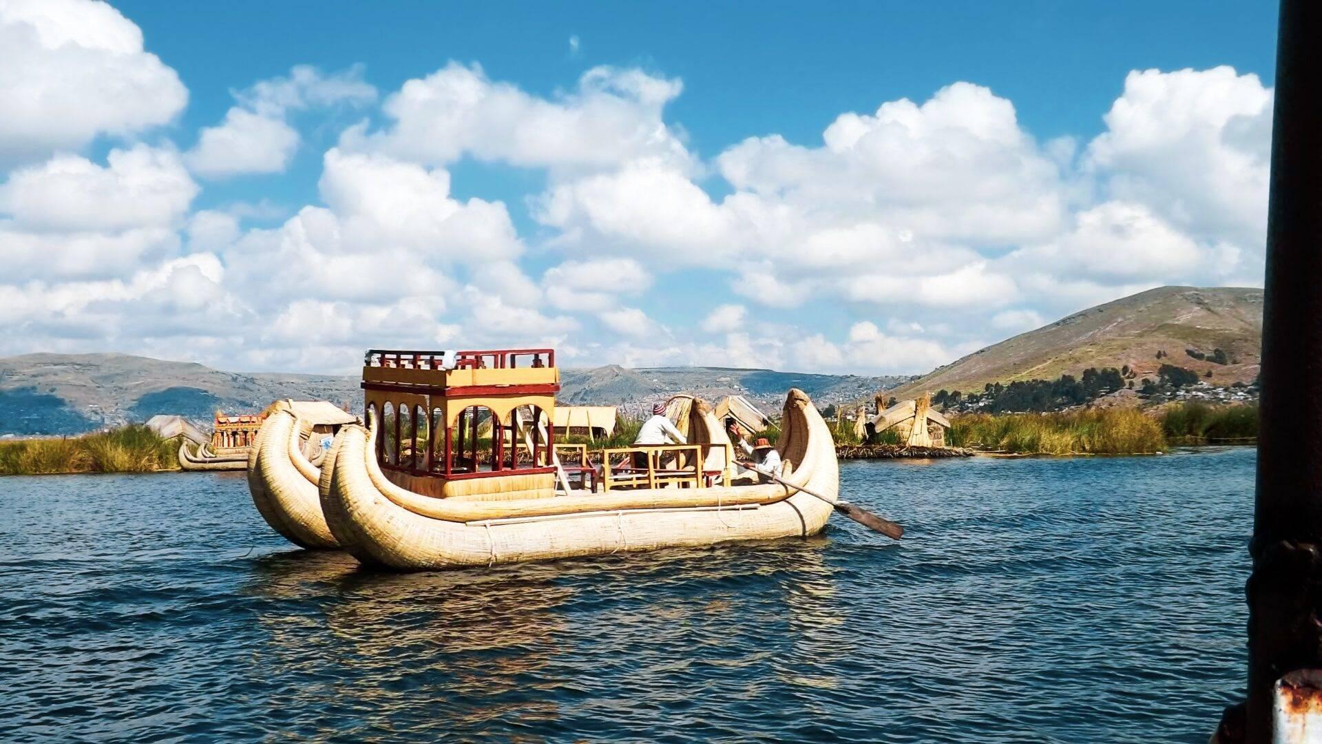 Una embarcación tradicional de totora con cabina roja navega sobre un lago de altitud rodeado de montañas áridas