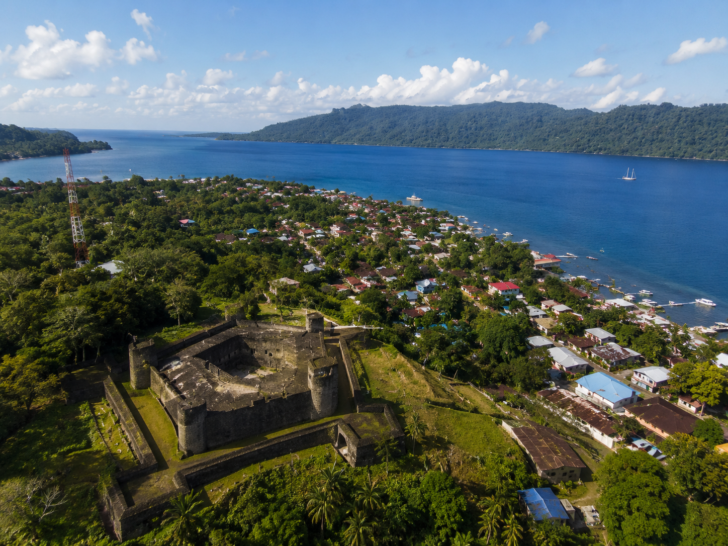 Koloniale Festung mit Blick auf eine türkisfarbene Bucht mit Küstendorf und dichtem Tropenwald
