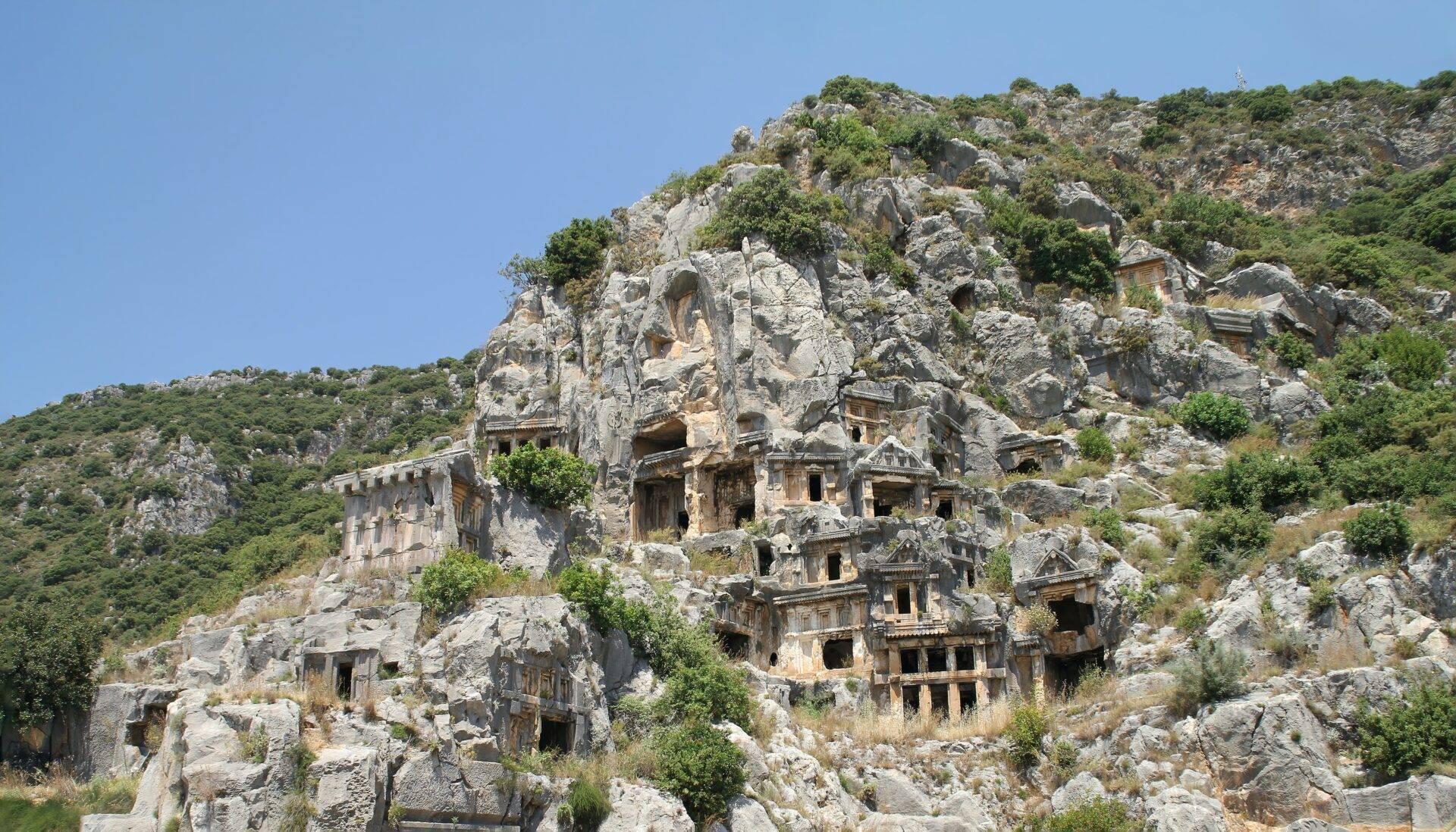 Antiche tombe rupestri scavate in una falesia rocciosa sotto un cielo blu sgombro