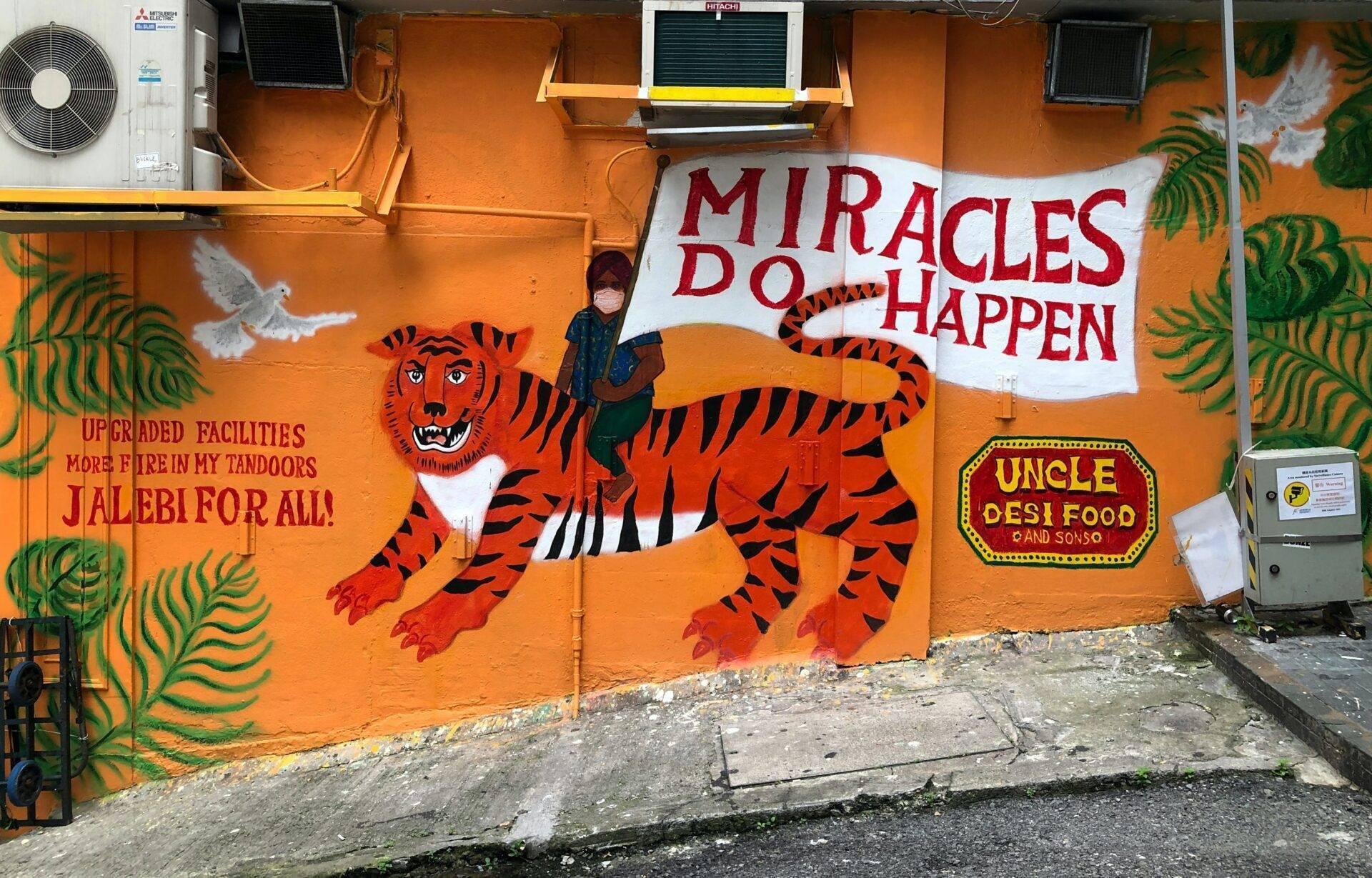 Orangefarbene bunte Fassade mit einem rot-schwarz gemalten Tiger, einer Frau davor und Restaurantschildern