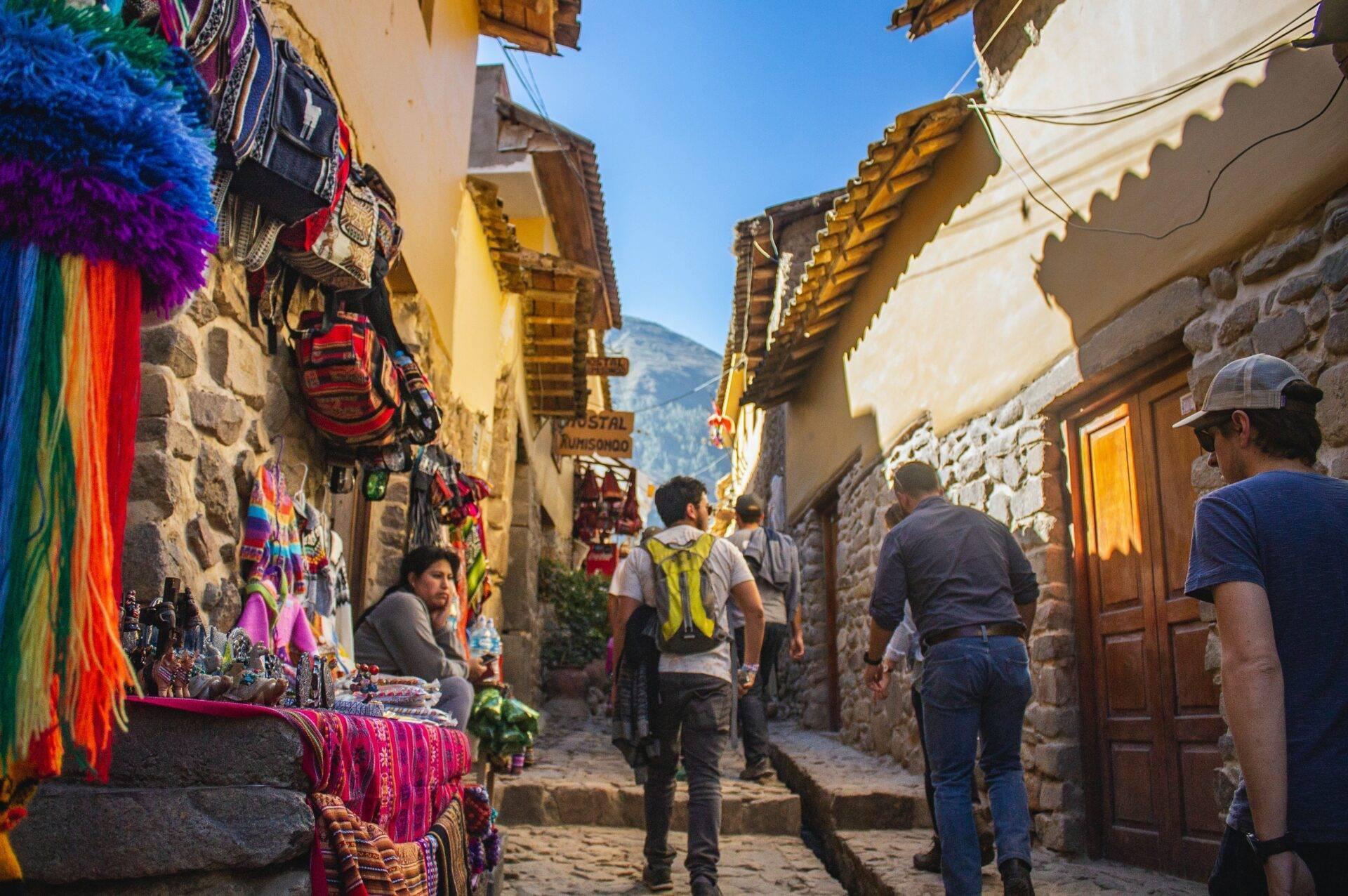 Una calle empedrada estrecha con tiendas de textiles coloridos y turistas paseando bajo tejados decorados de madera