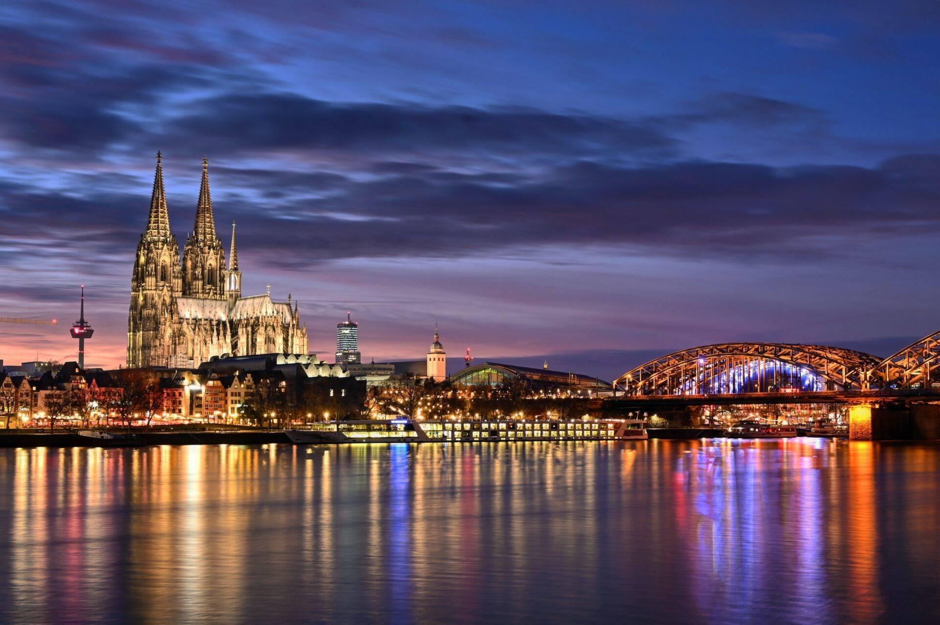 Cattedrale gotica illuminata al tramonto con ponte in acciaio e riflessi nel fiume in serata