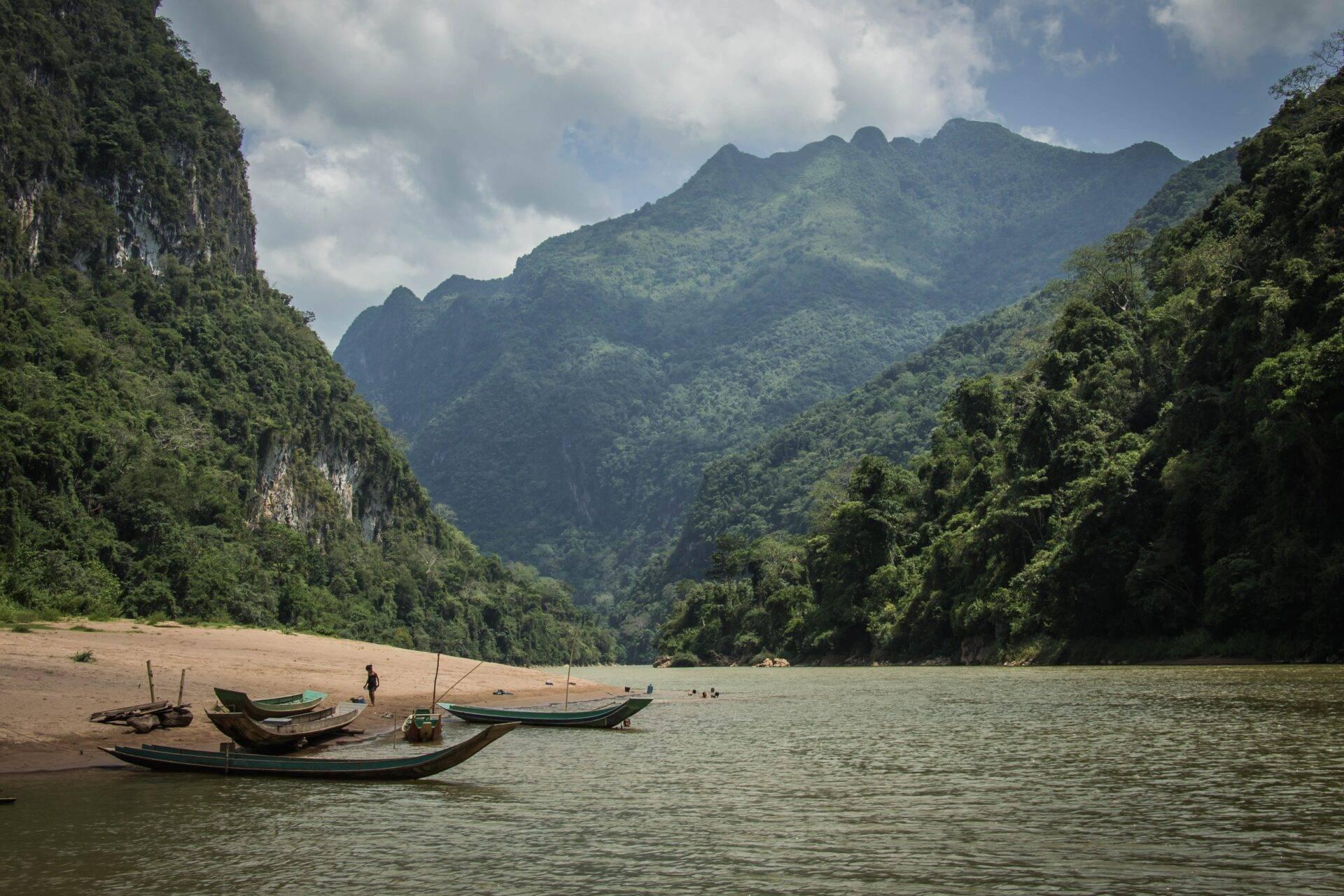 Reisender blickt auf den Mekong in Laos, traditionelles Einbaupiroge im Vordergrund