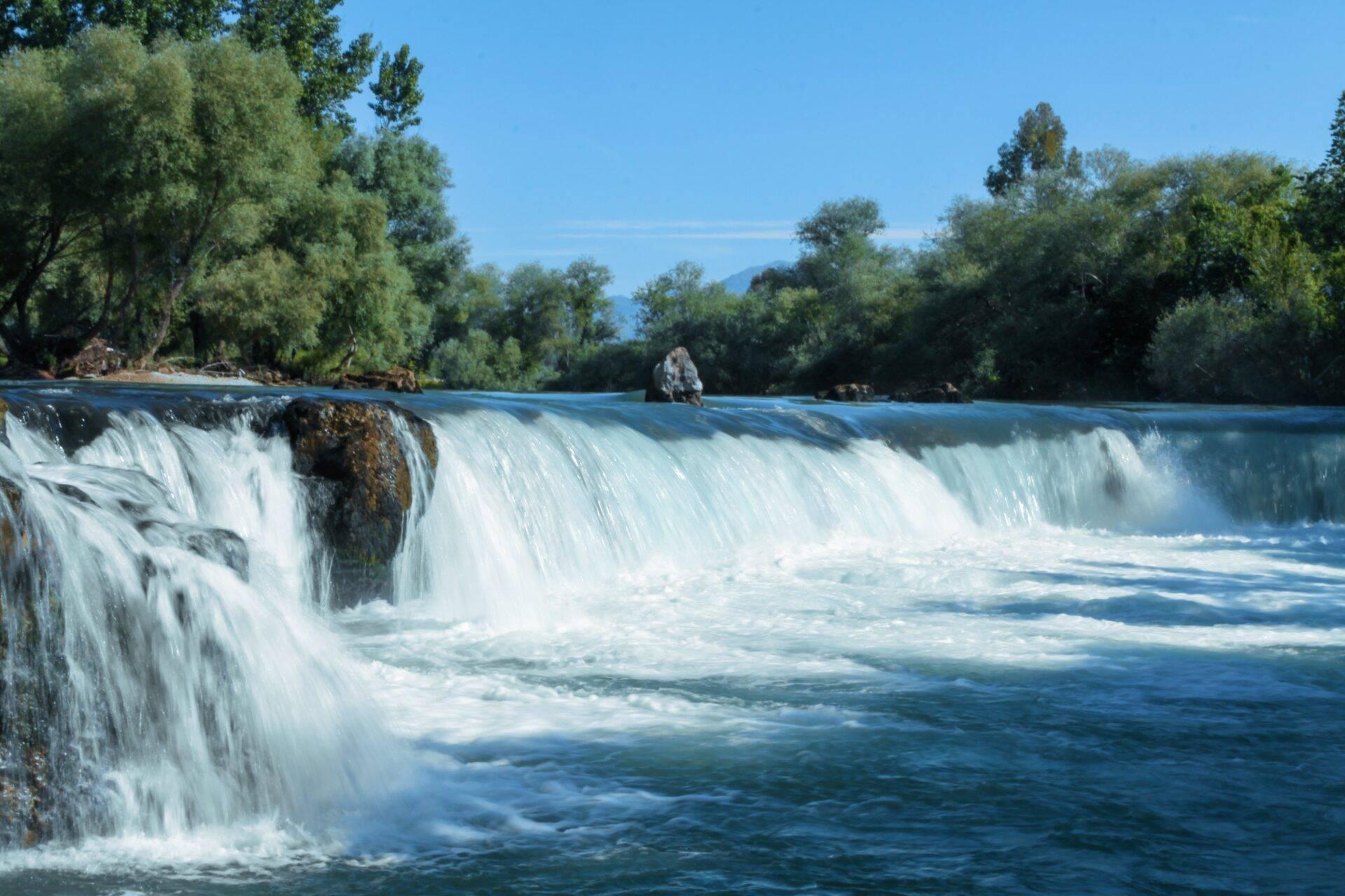 Una cascata spettacolare si riversa in un fiume turchese circondato da vegetazione lussureggiante e montagne