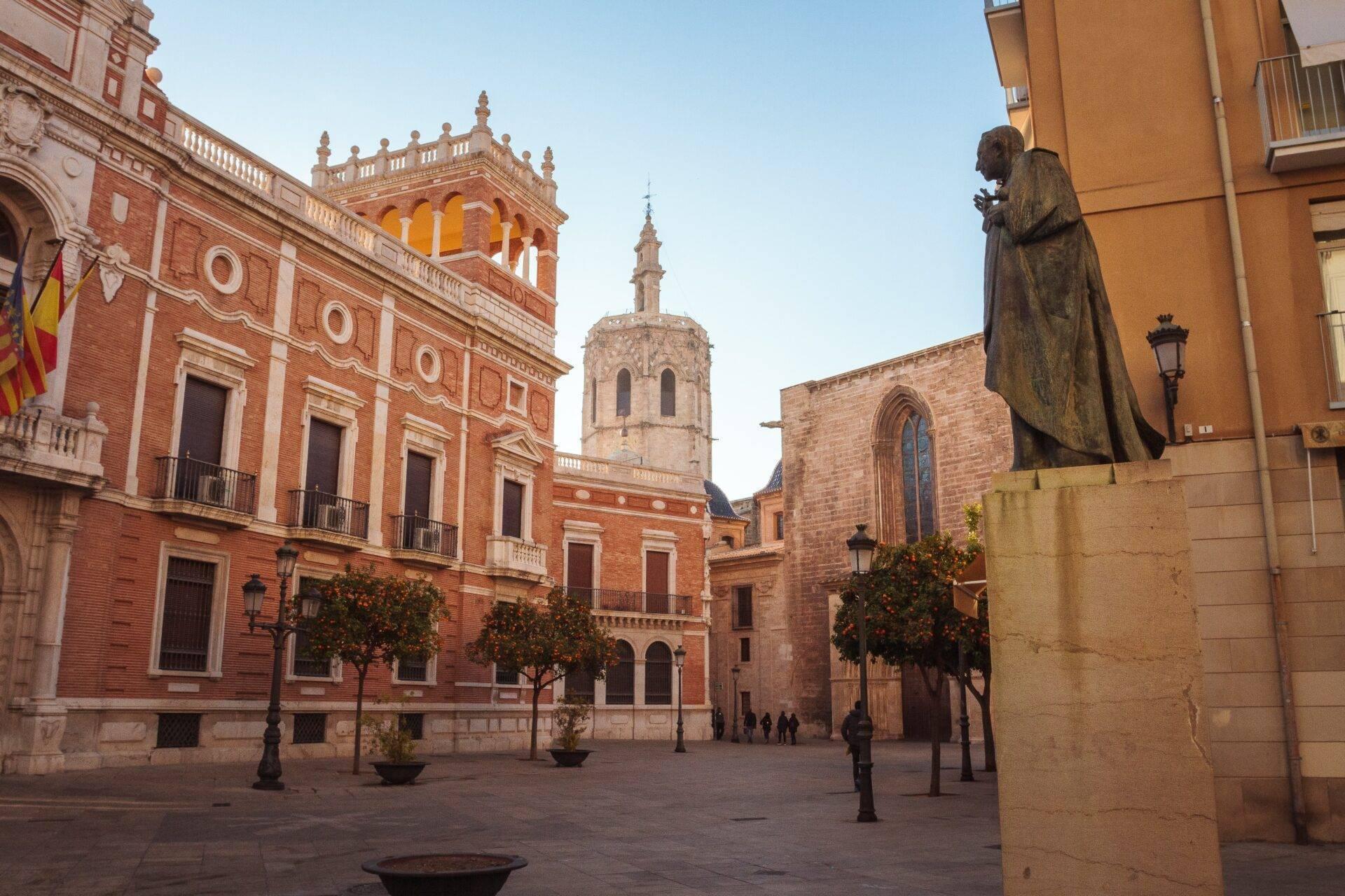 Una piazza storica in Spagna con edifici in mattoni rossi, chiesa e statua monumentale sotto un cielo terso