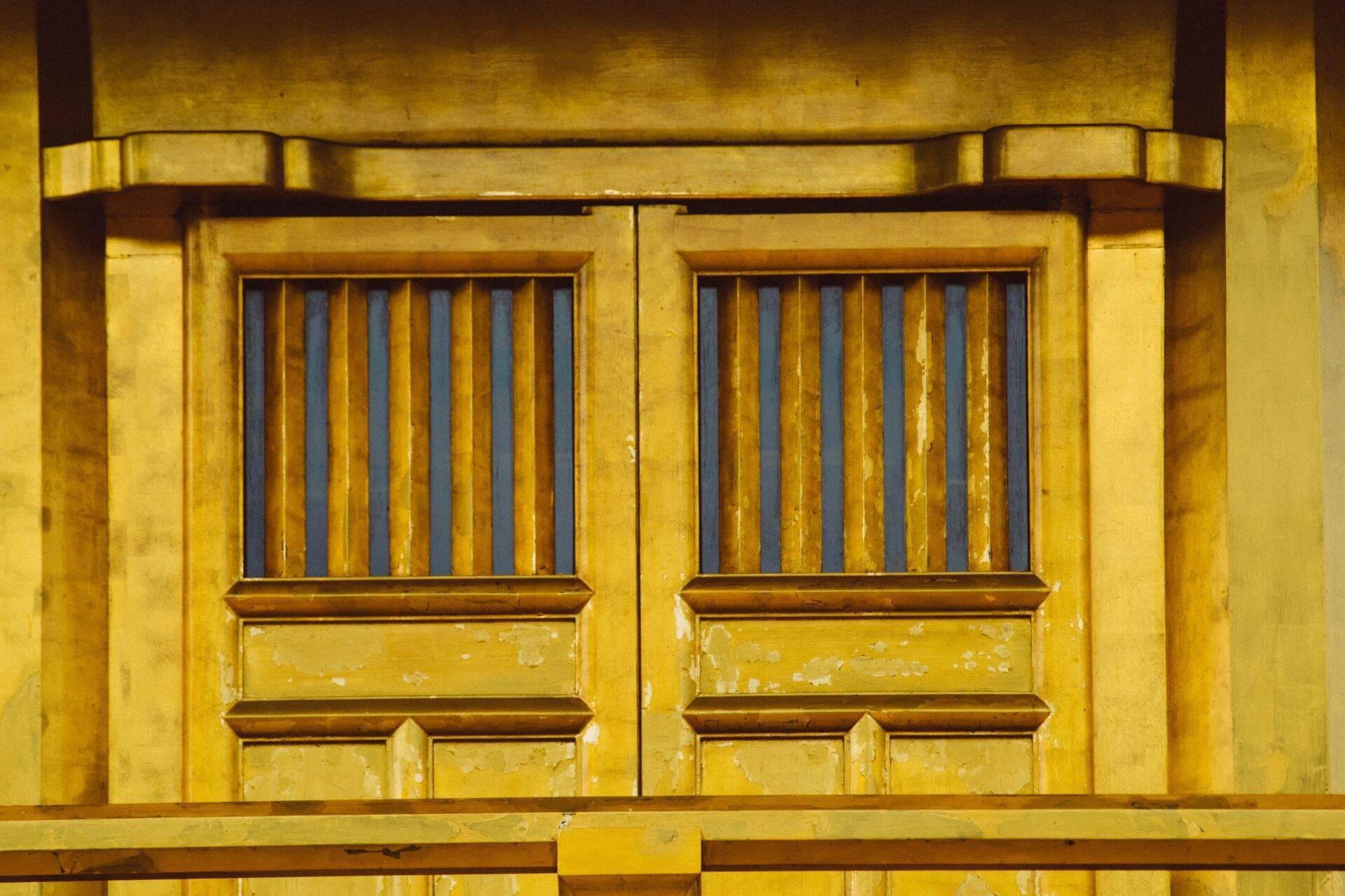 Gelb-koloniale Fassade mit zwei vergitterten Metalltüren und bemalten Tafeln, historische asiatische Architektur