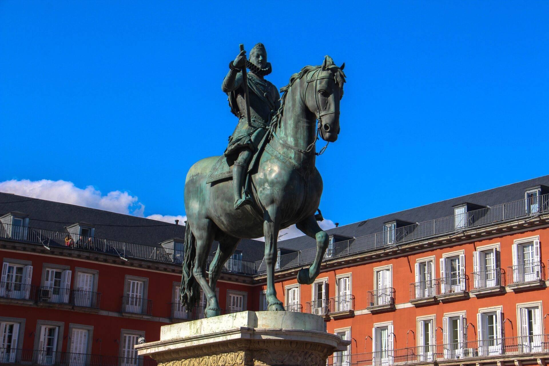 Statua equestre in bronzo in una piazza circondata da edifici coloniali rossi sotto un cielo azzurro
