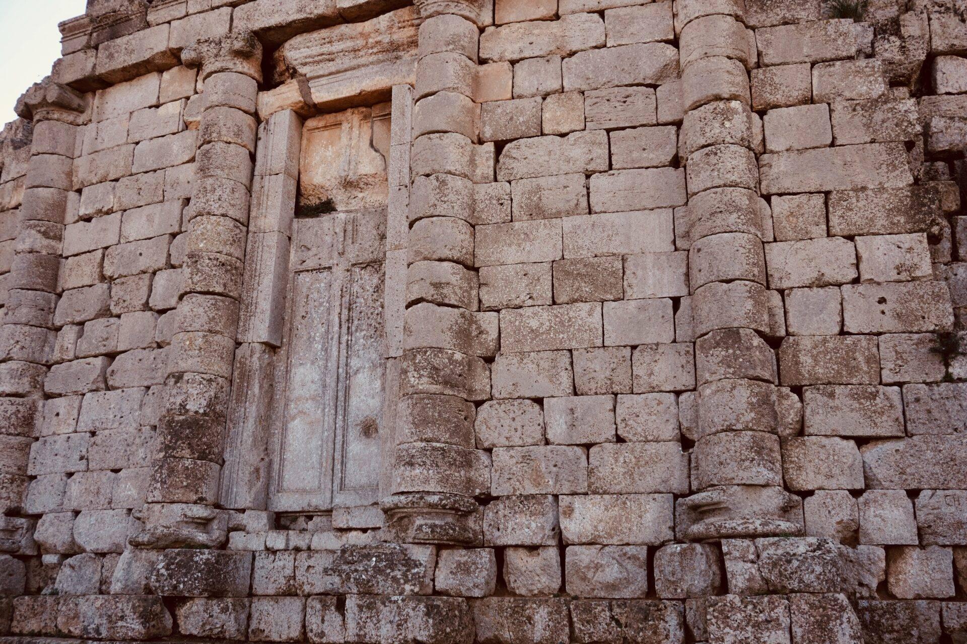 Dettaglio di una facciata in pietra antica con colonne cilindriche e portale architetturato, testimonianza dell’architettura storica