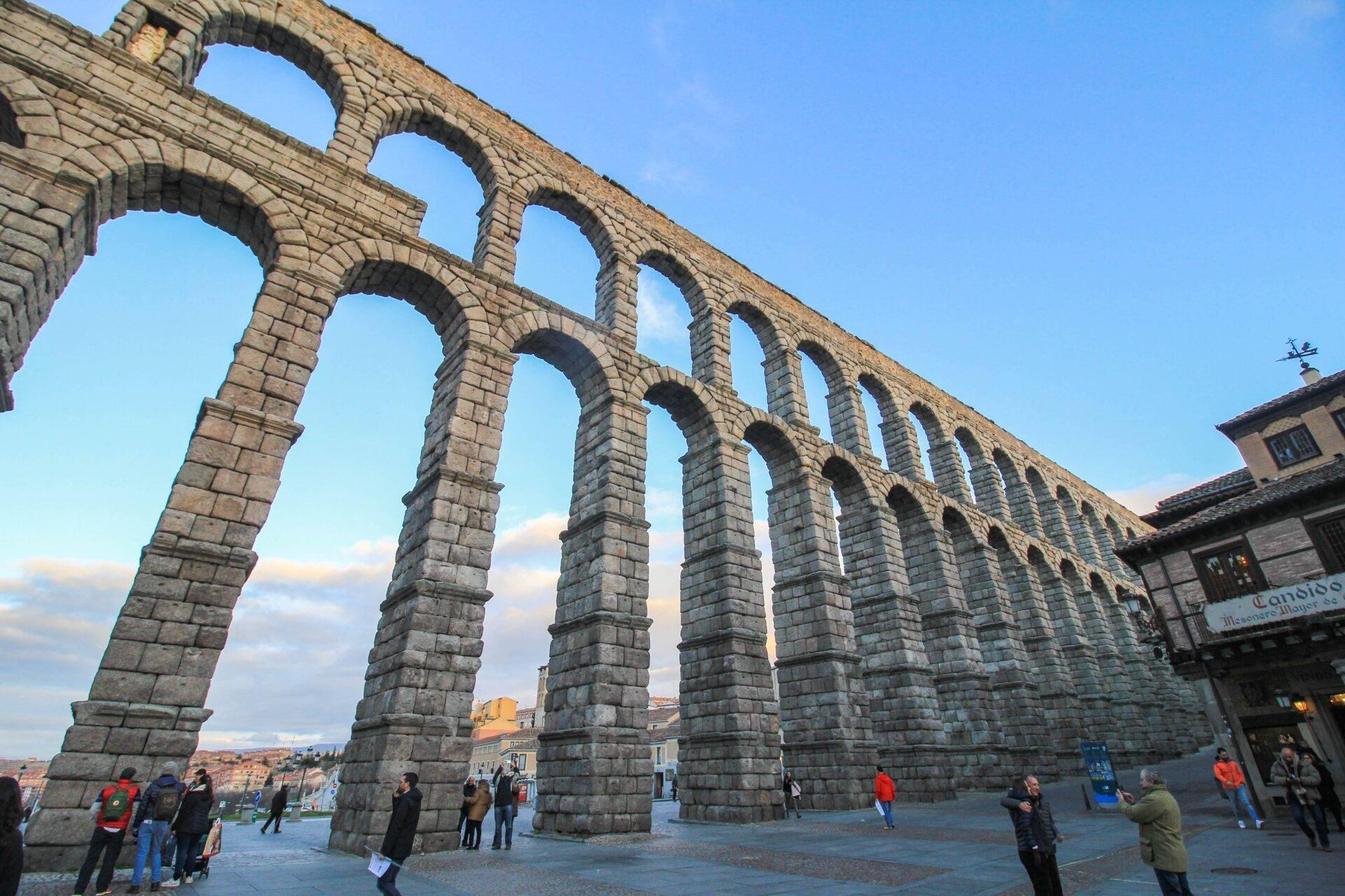 L’acquedotto romano di Segovia con le sue monumentali arcate in pietra e visitatori che passeggiano sulla piazza
