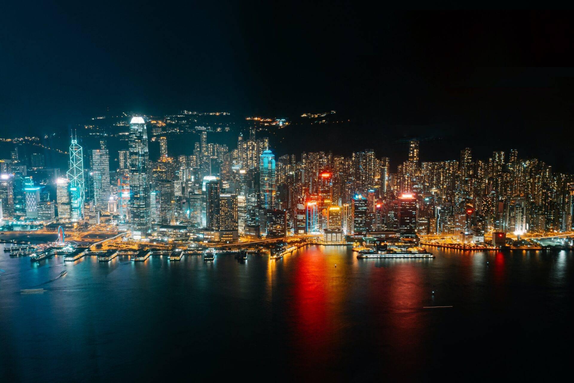 Nächtliche Skyline einer Küstenmetropole mit beleuchteten Wolkenkratzern, die sich im Wasser spiegeln