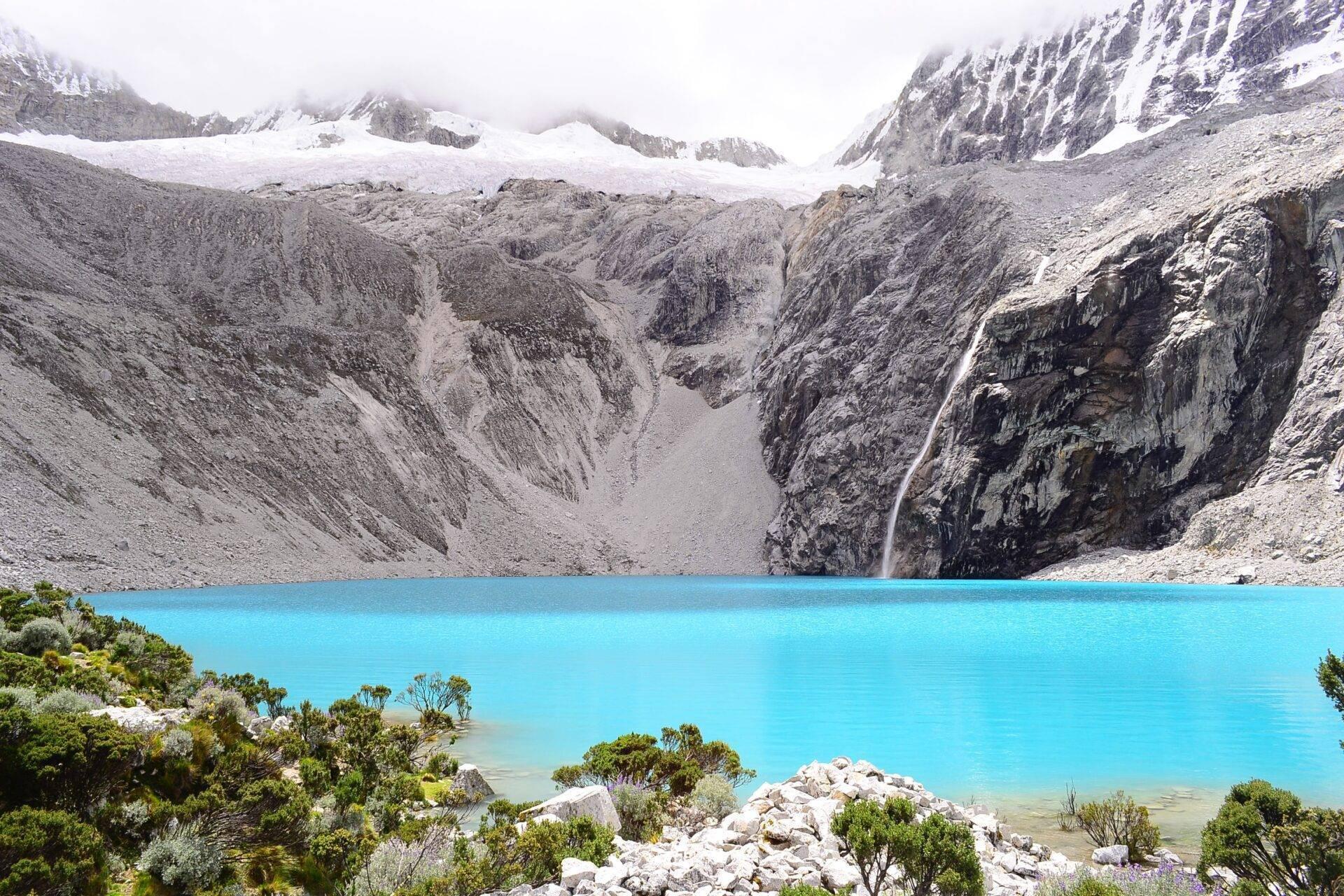 Lago de montaña de un azul turquesa intenso rodeado de picos nevados, glaciar y cascada en un paisaje alpino