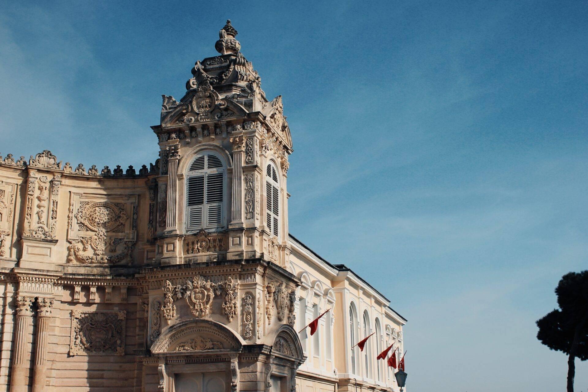 Facciata ornamentata di un edificio storico con torre elaborata e bandiere rosse sotto un cielo blu