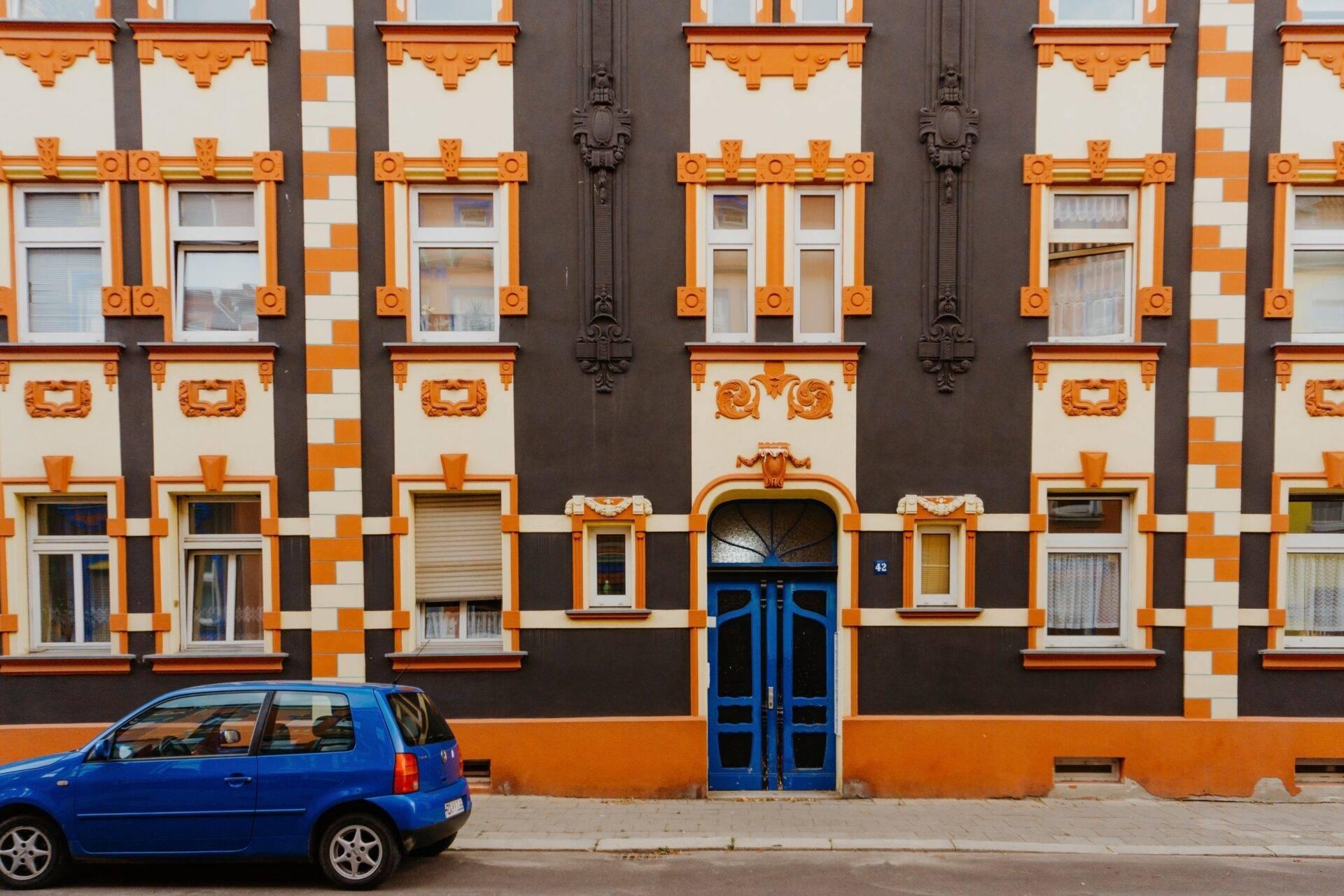 Facciata colorata di un edificio Art Déco arancione e nero con un’auto blu parcheggiata davanti