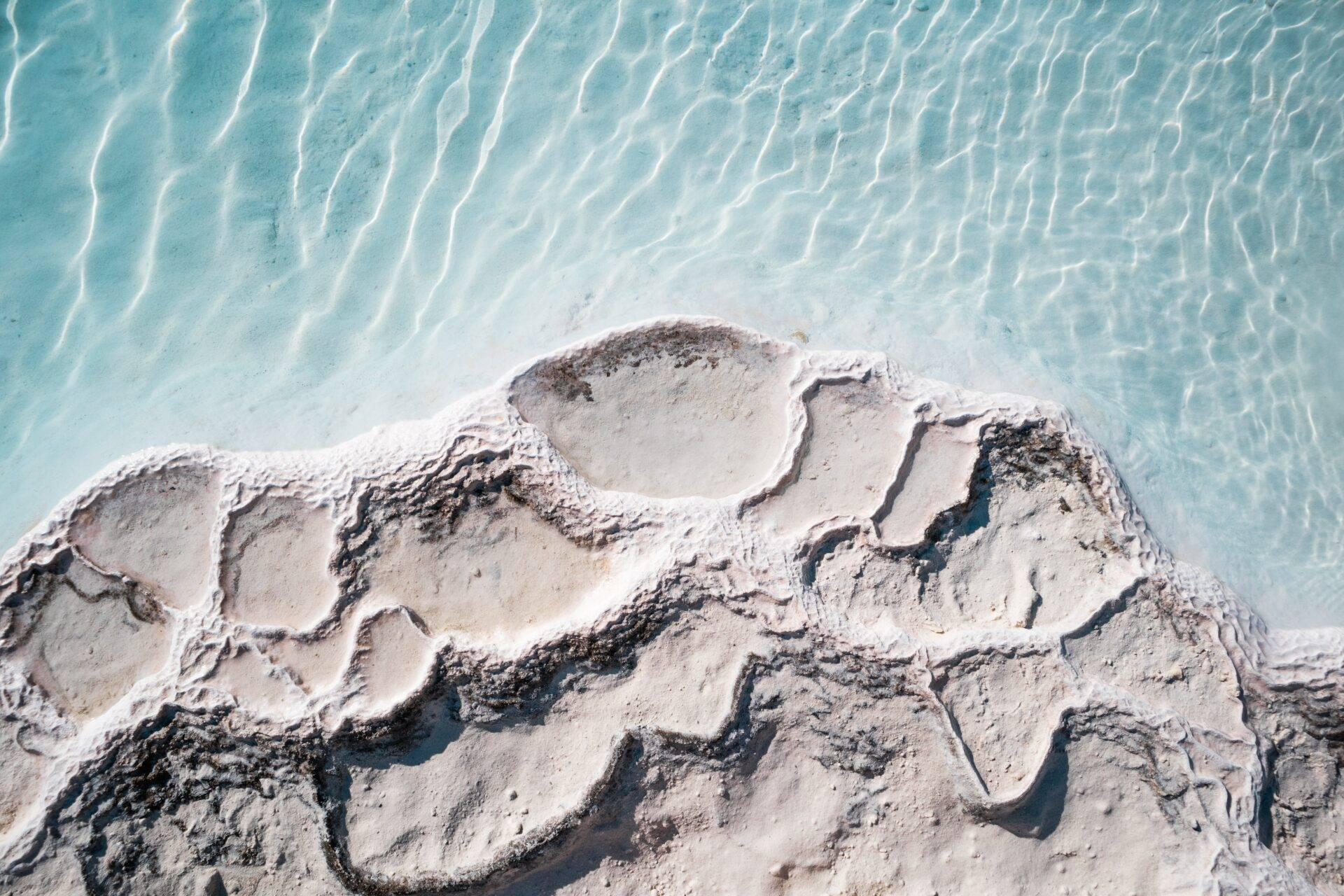 Vista aerea di una formazione geologica bianca e corrosa bordata da un’acqua turchese cristallina