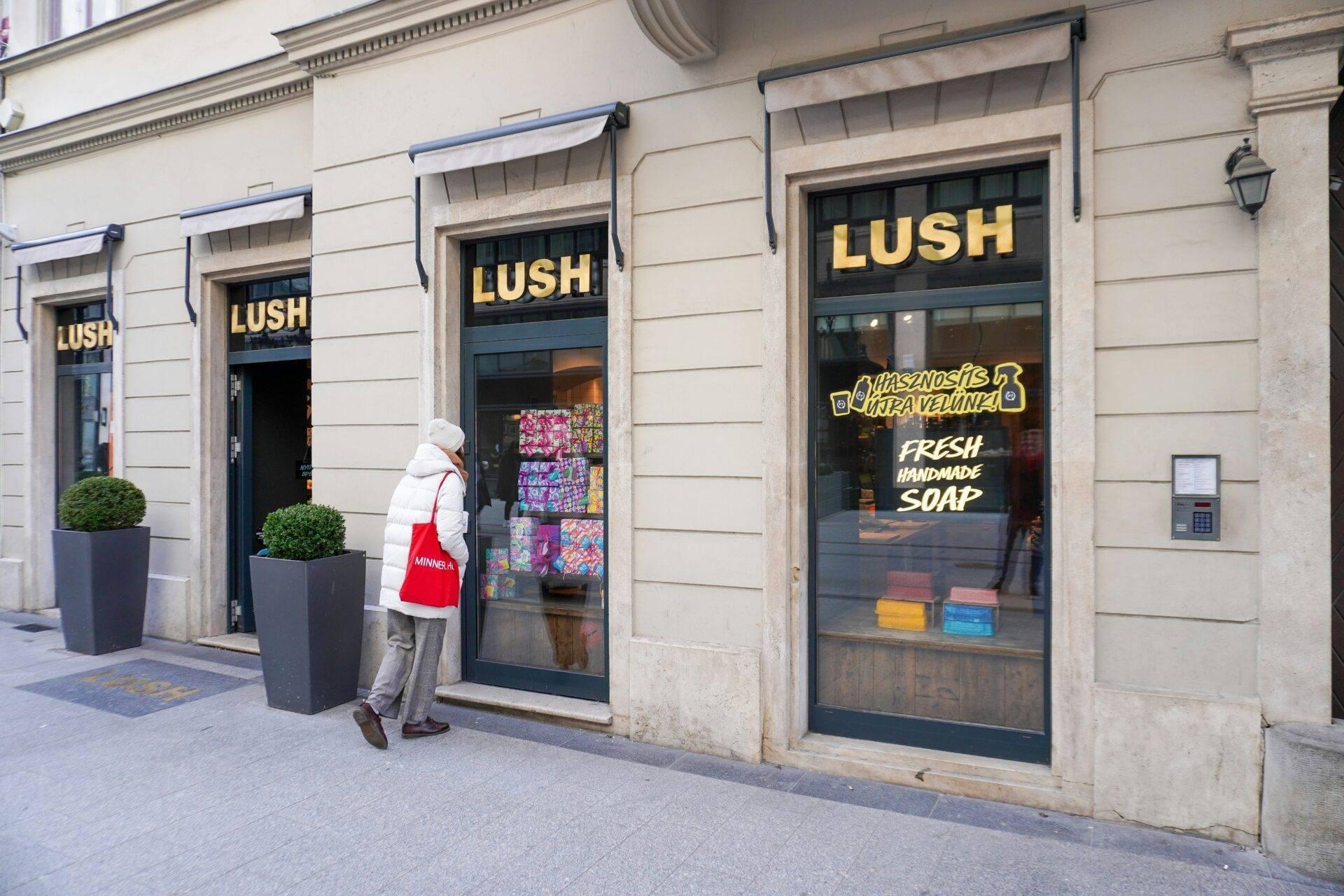 Una mujer frente a una tienda de cosméticos artesanales en una calle adoquinada europea con fachada clásica