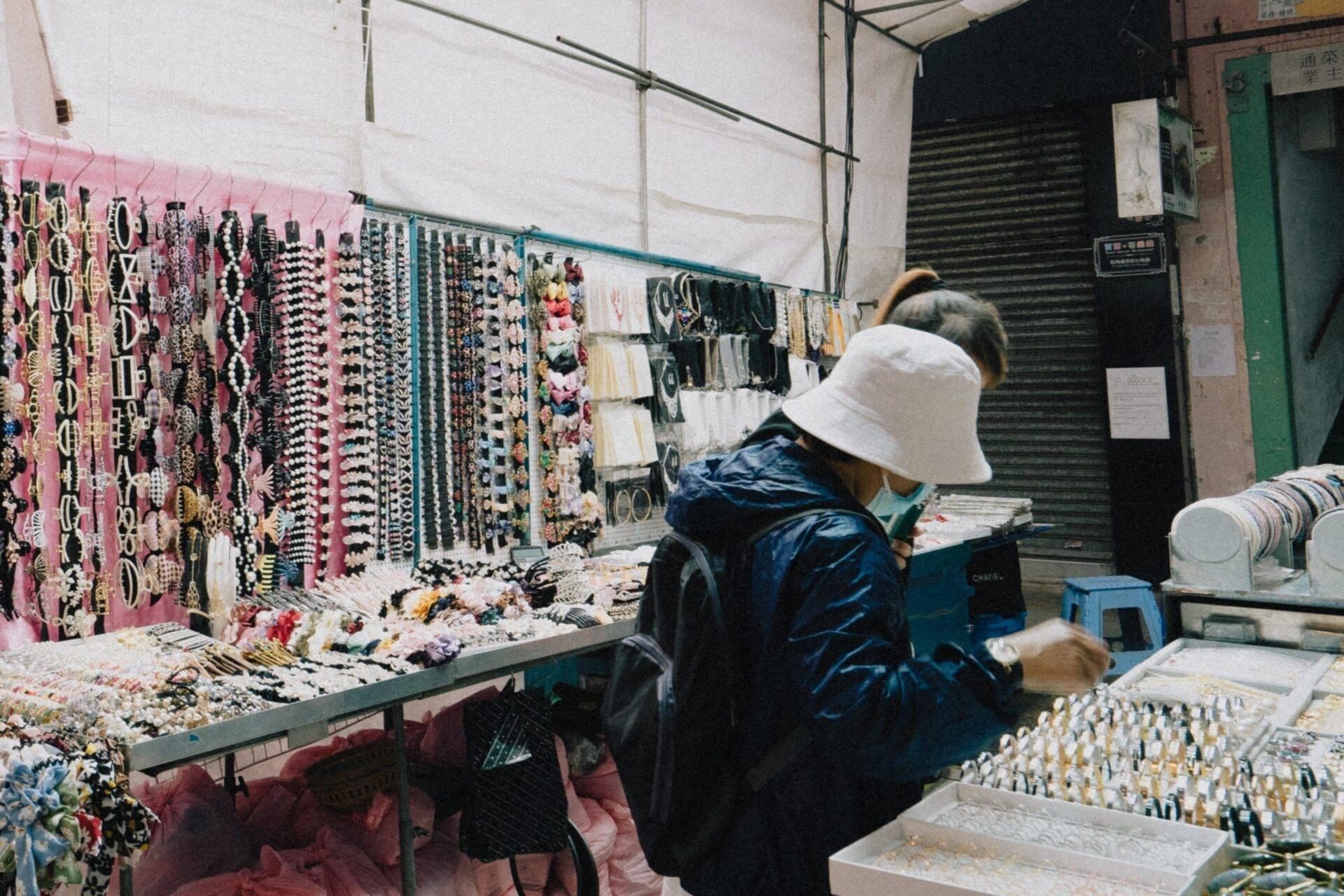 Schmuckverkäuferin in einem überdachten asiatischen Markt, die bunte Halsketten und Armbänder präsentiert