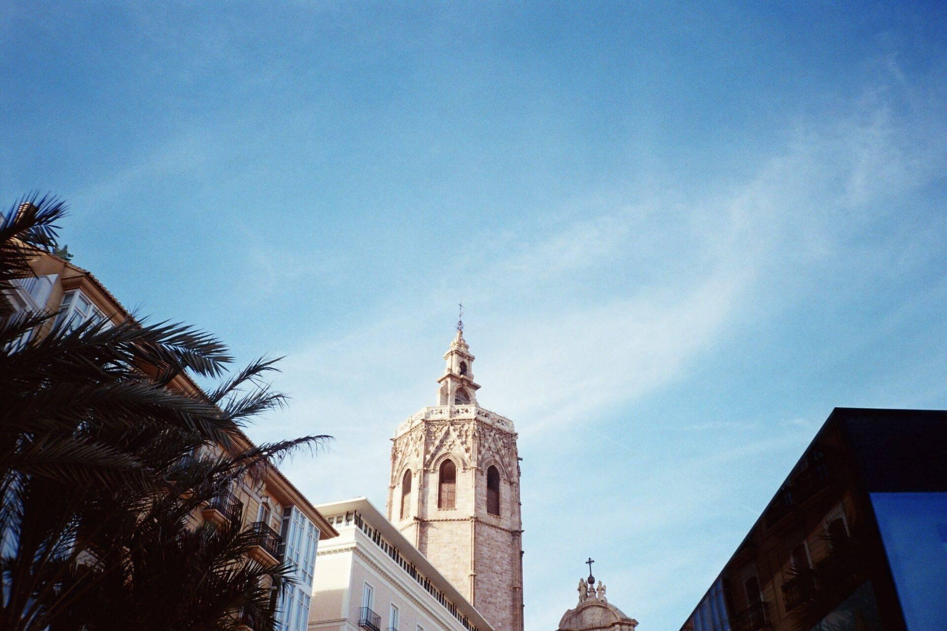 Campanile barocco di una chiesa spagnola incorniciato da palme e palazzi coloniali sotto un cielo azzurro