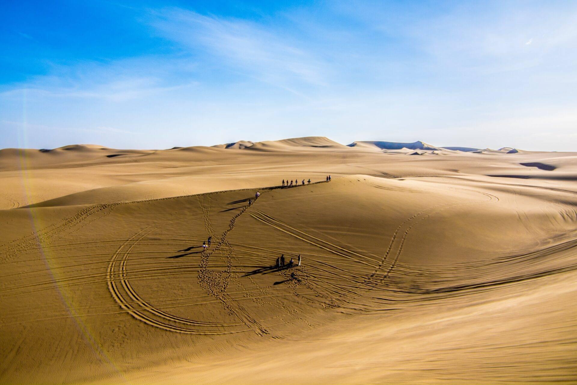 Viajeros caminando en caravana a través de las dunas de arena de un vasto desierto árido bajo un cielo azul