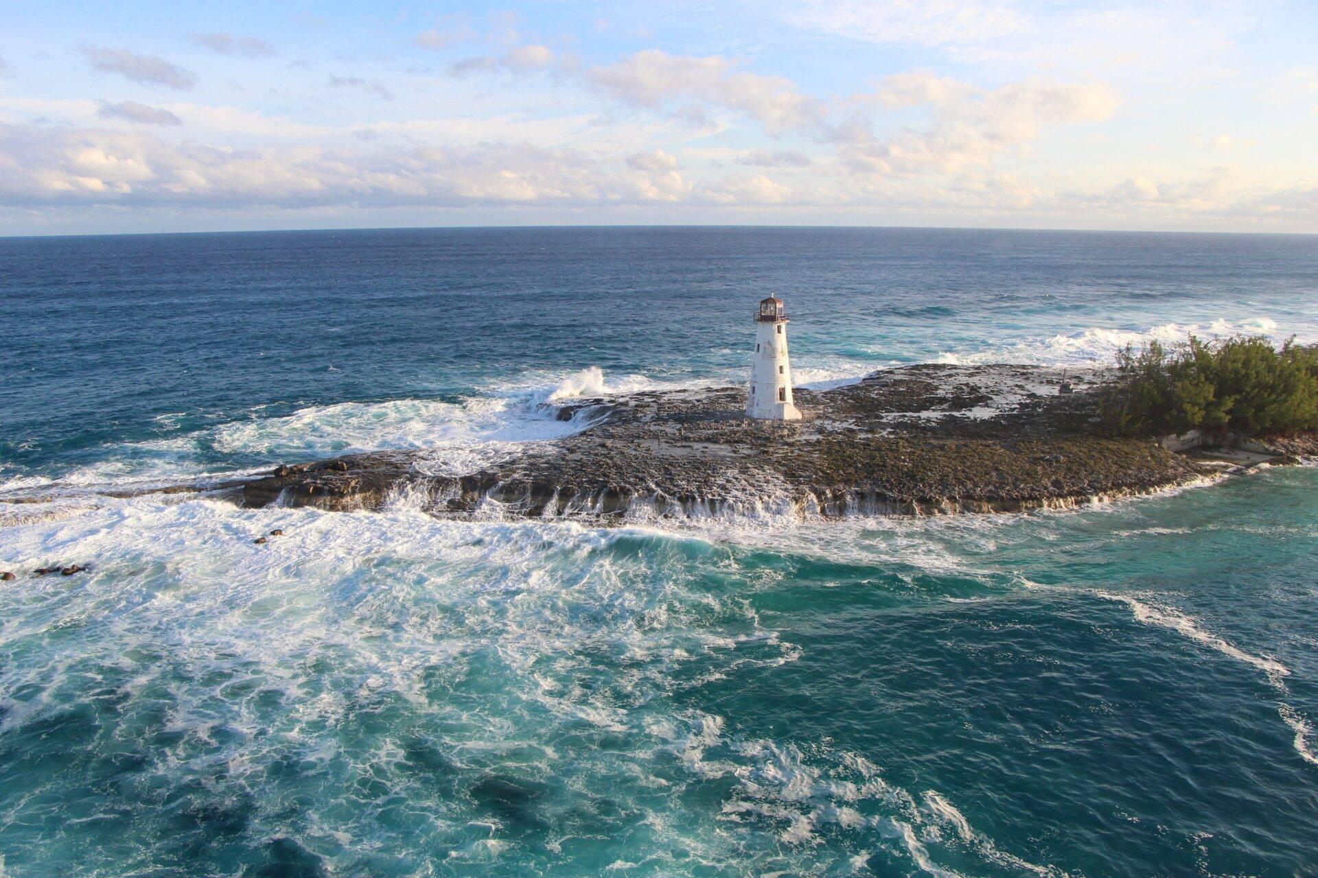 Faro blanco sobre una punta rocosa azotada por las olas del océano turquesa en Bahamas