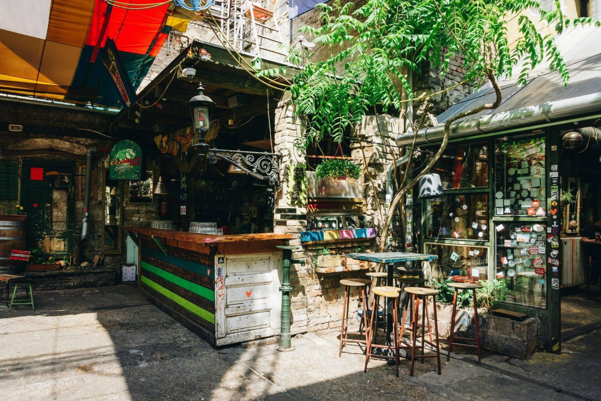 Un patio interior bohemio con bar colorido, vegetación trepadora y mobiliario vintage en un ambiente urbano alternativo