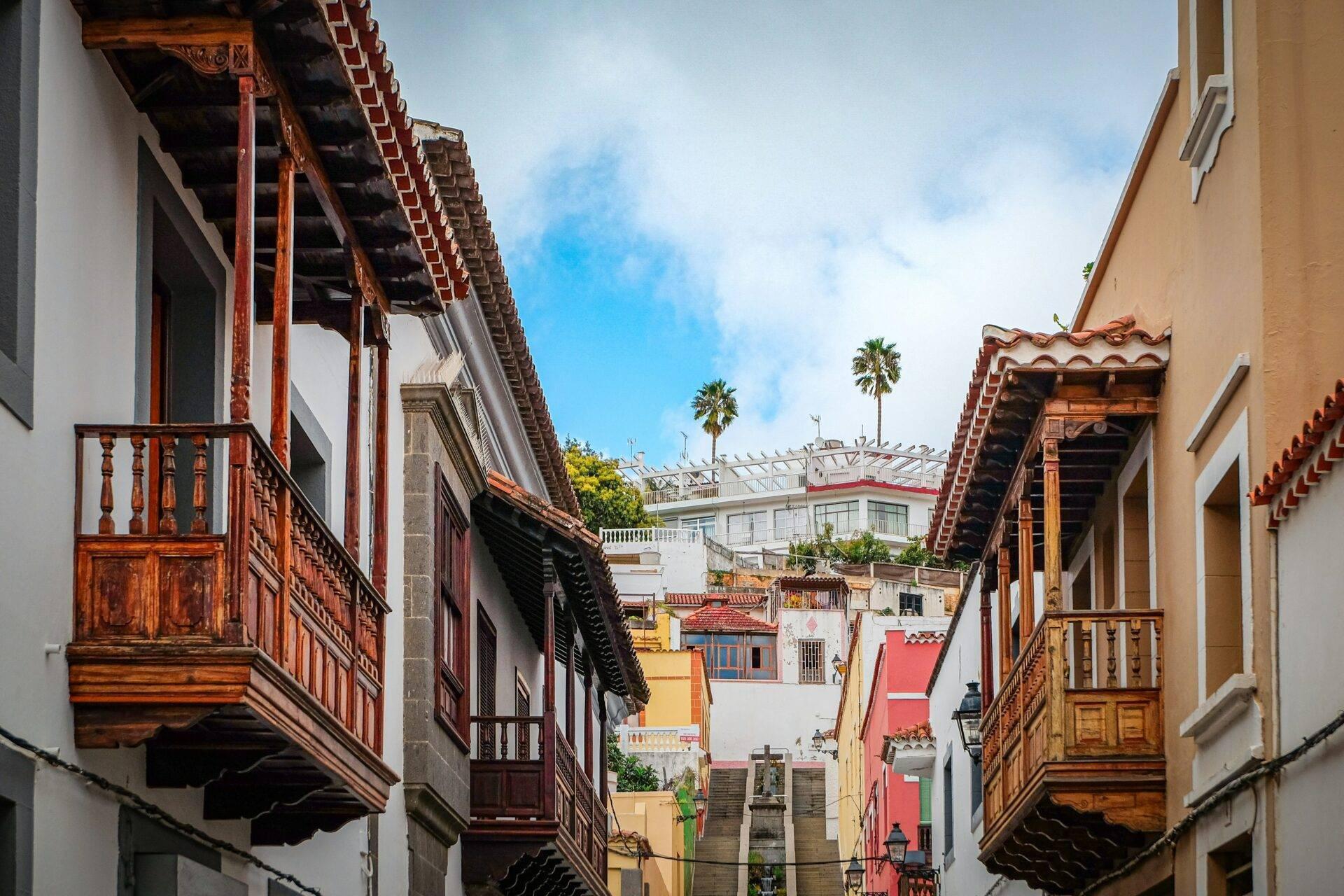 Calle empedrada estrecha con balcones de madera de colores, casas coloniales y palmeras bajo cielo azul