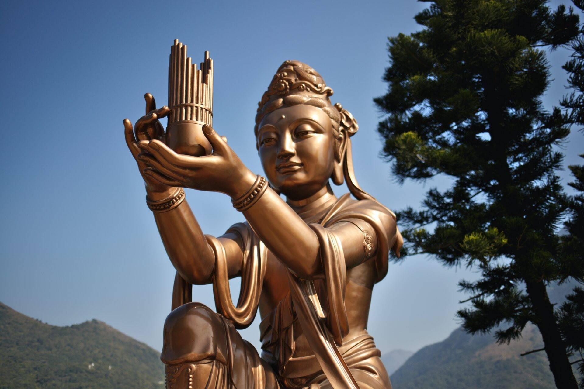 Vergoldete Statue einer buddhistischen Göttin mit rituellem Krug in einer bewaldeten Berglandschaft