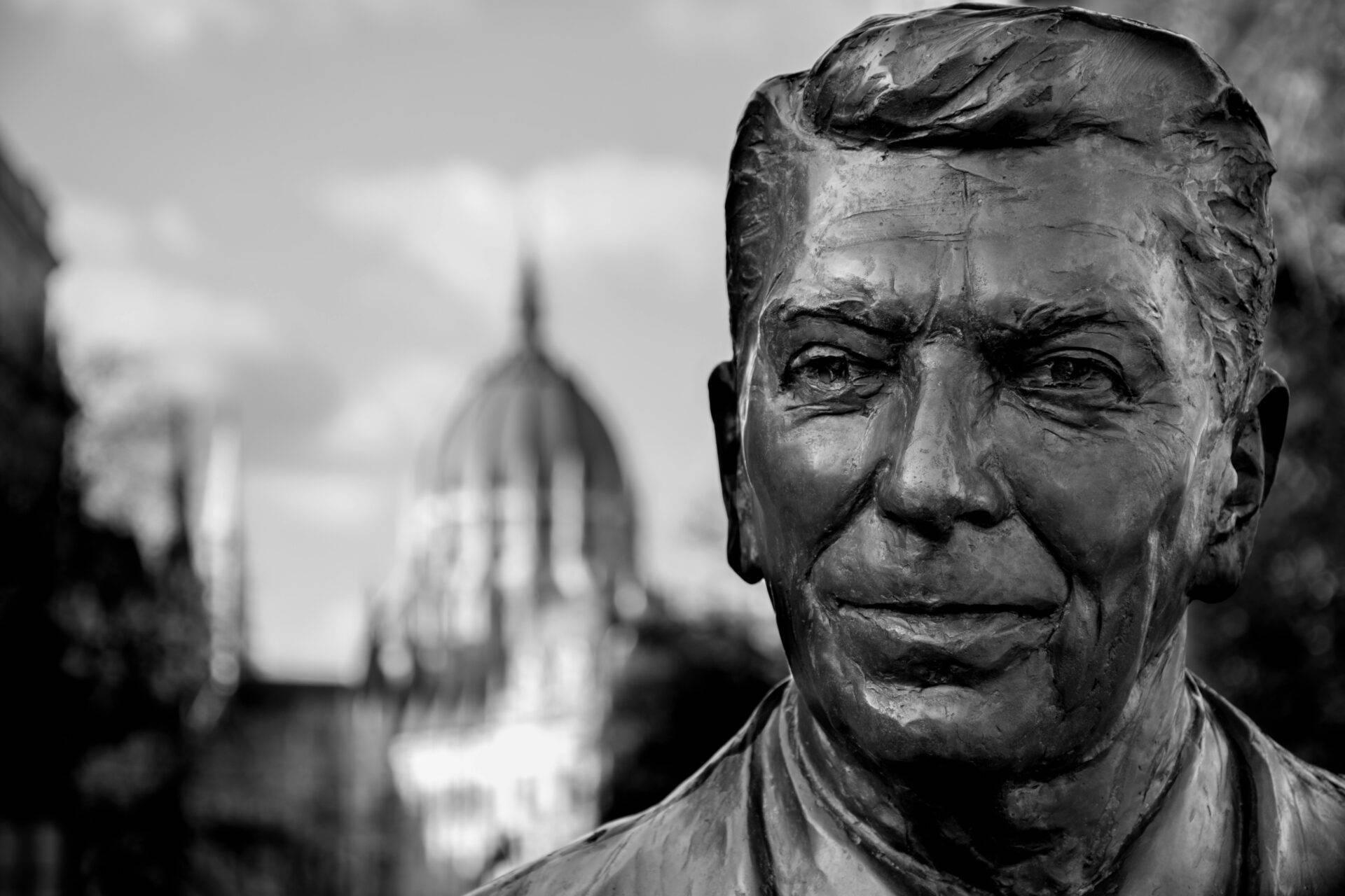 Estatua de bronce de un hombre con edificio religioso de cúpula al fondo, ambiente urbano invernal