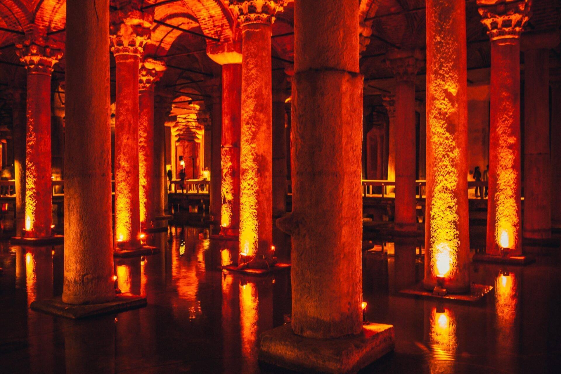 Una basilica sotterranea illuminata in rosso-arancione con imponenti colonne e i loro riflessi nell’acqua