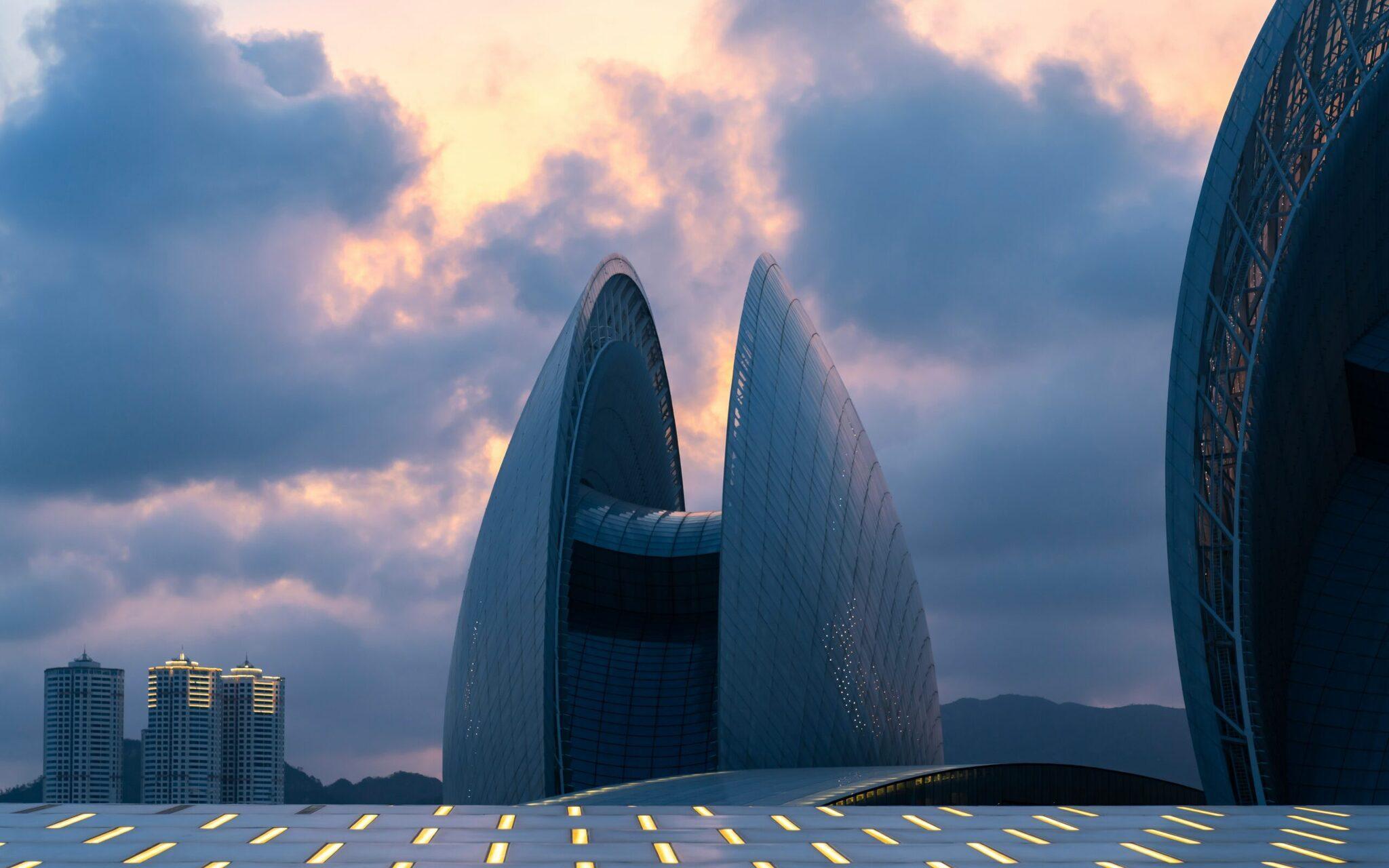 Arquitectura moderna futurista con edificios en forma de vela al atardecer, rodeados de rascacielos