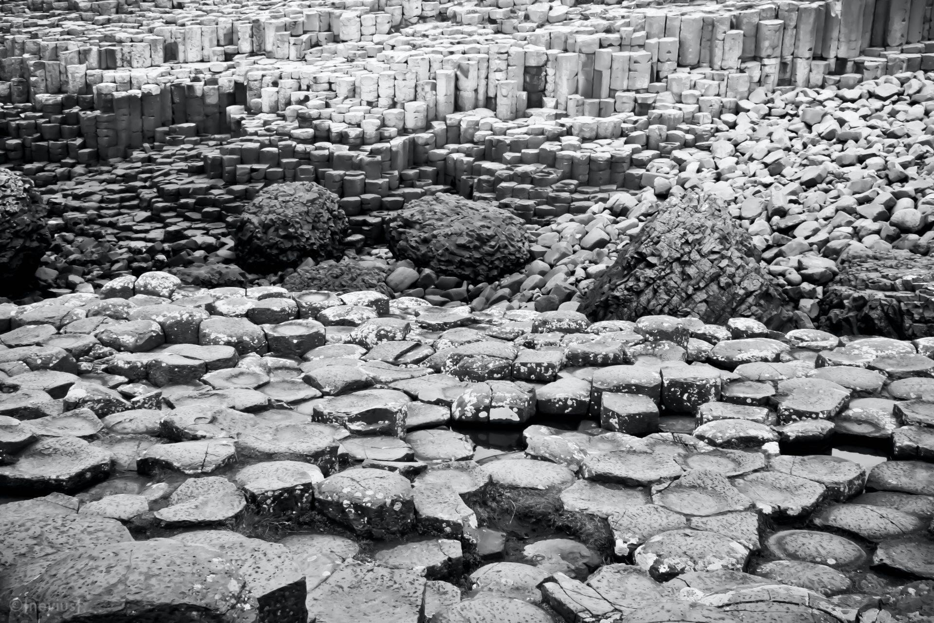 Nahaufnahme grauer hexagonaler Basaltsäulenformationen an einem felsigen Strand
