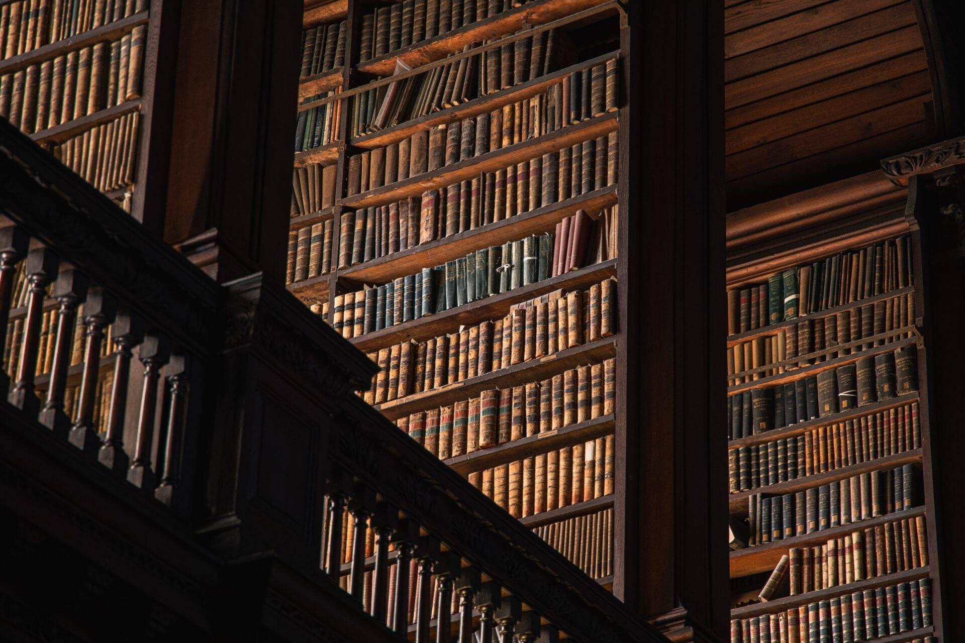 Inneres einer historischen Bibliothek mit hölzernen Bücherregalen voller alter Bücher, Holztreppe und natürlichem Licht
