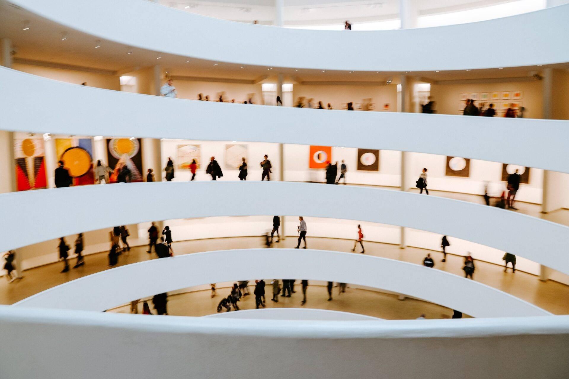 Vista dall’alto di un museo dalle spirali bianche con visitatori che passeggiano e opere d’arte colorate esposte