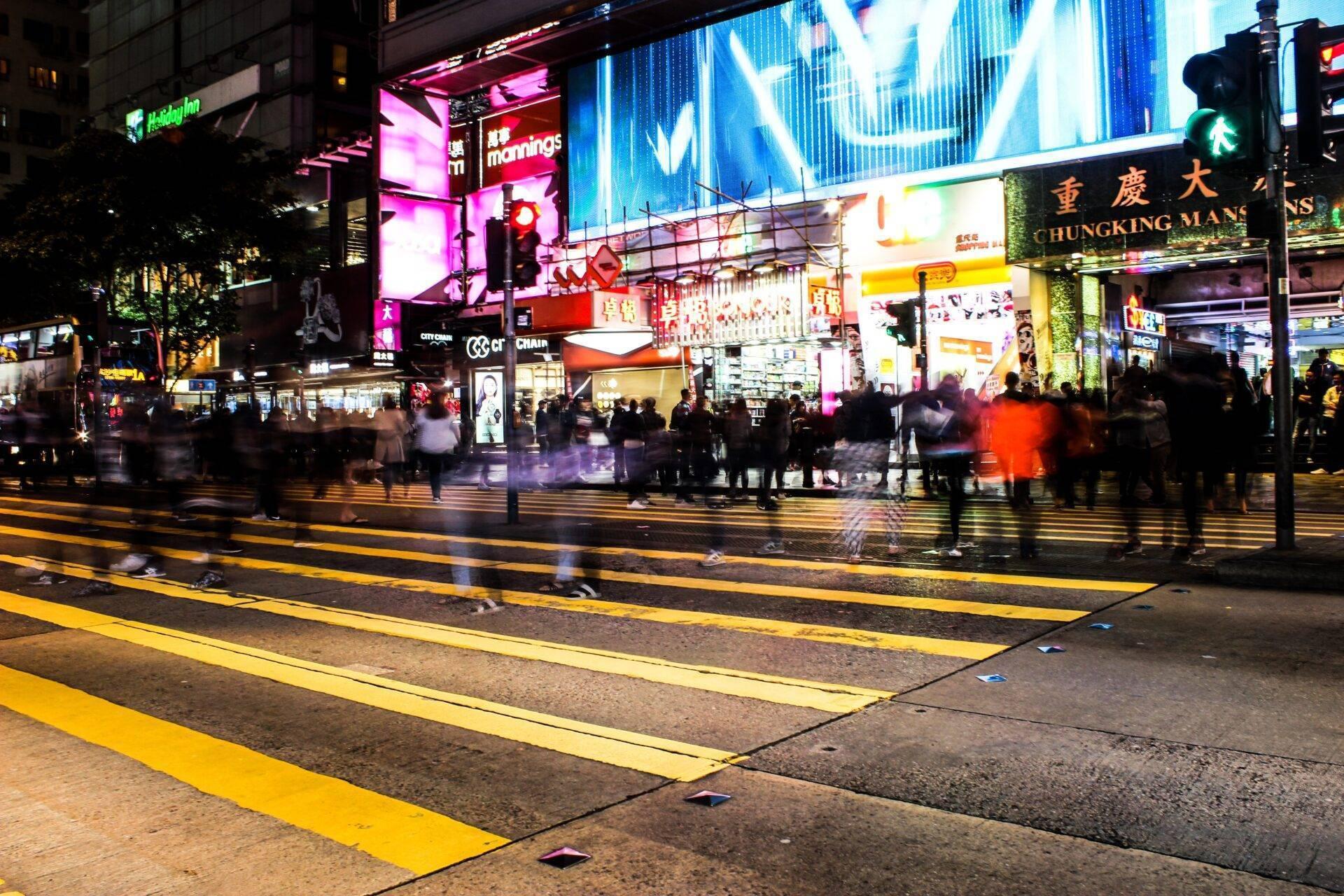 Belebte Einkaufsstraße bei Nacht mit Leuchtreklamen, Fußgängerüberwegen und Menschenmassen aus Touristen und Einheimischen