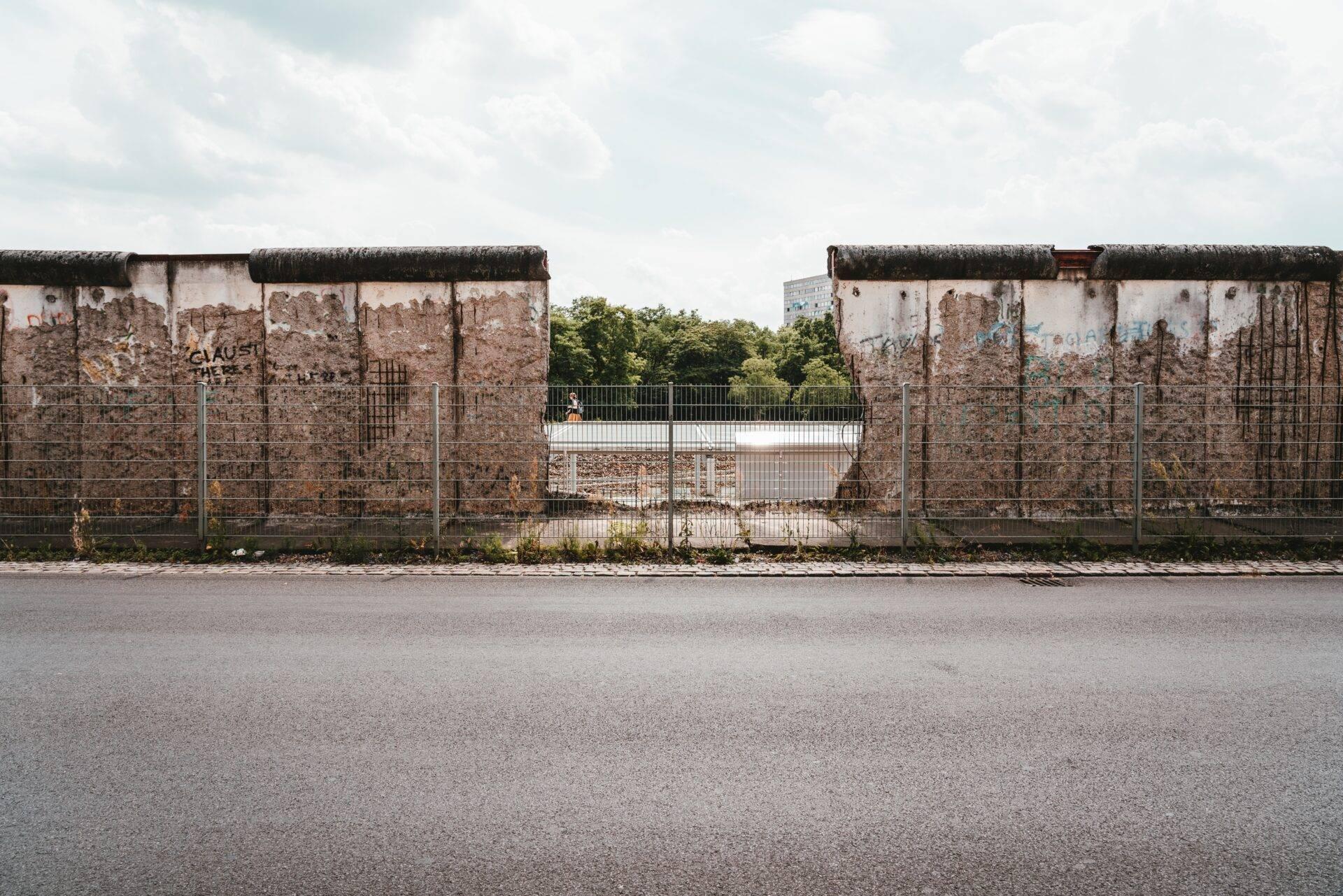 Resti del Muro di Berlino con mattoni a vista, graffiti e recinzione metallica in una giornata nuvolosa
