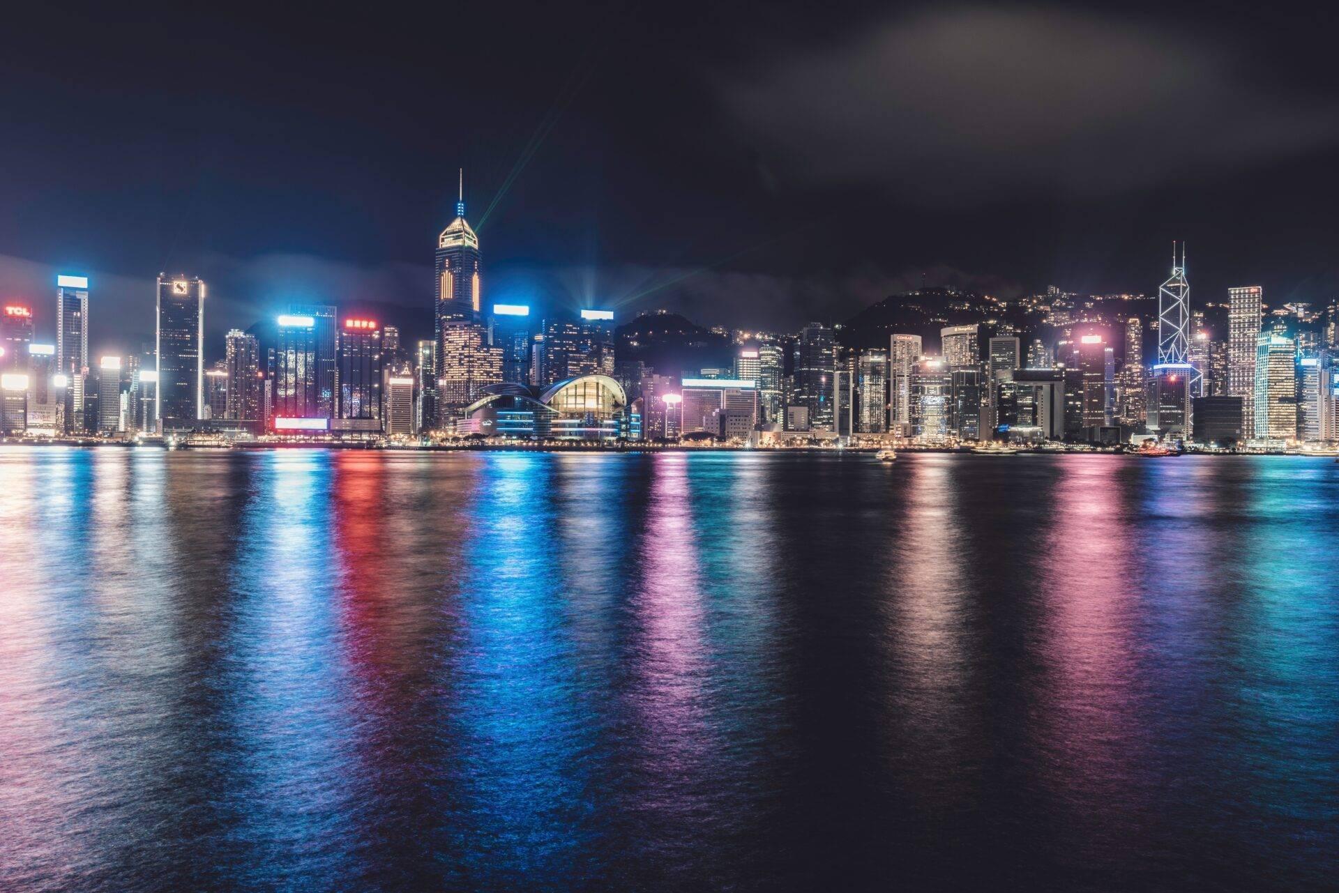 Beleuchtete Skyline einer Küstenmetropole bei Nacht mit Wolkenkratzern, die sich im ruhigen Wasser spiegeln
