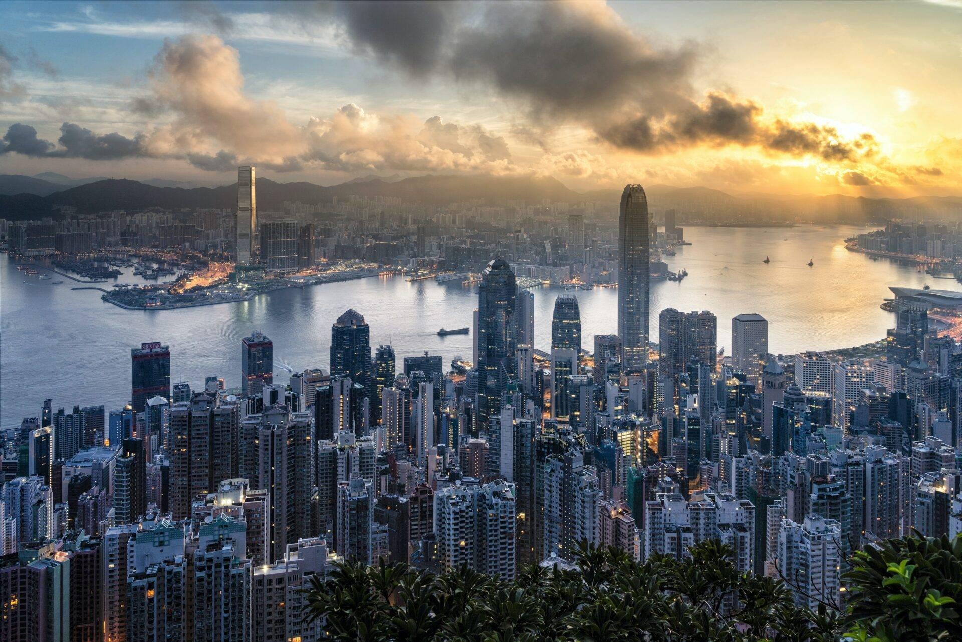 Luftaufnahme einer asiatischen Metropole im Sonnenuntergang mit Wolkenkratzern, Bucht und Bergen