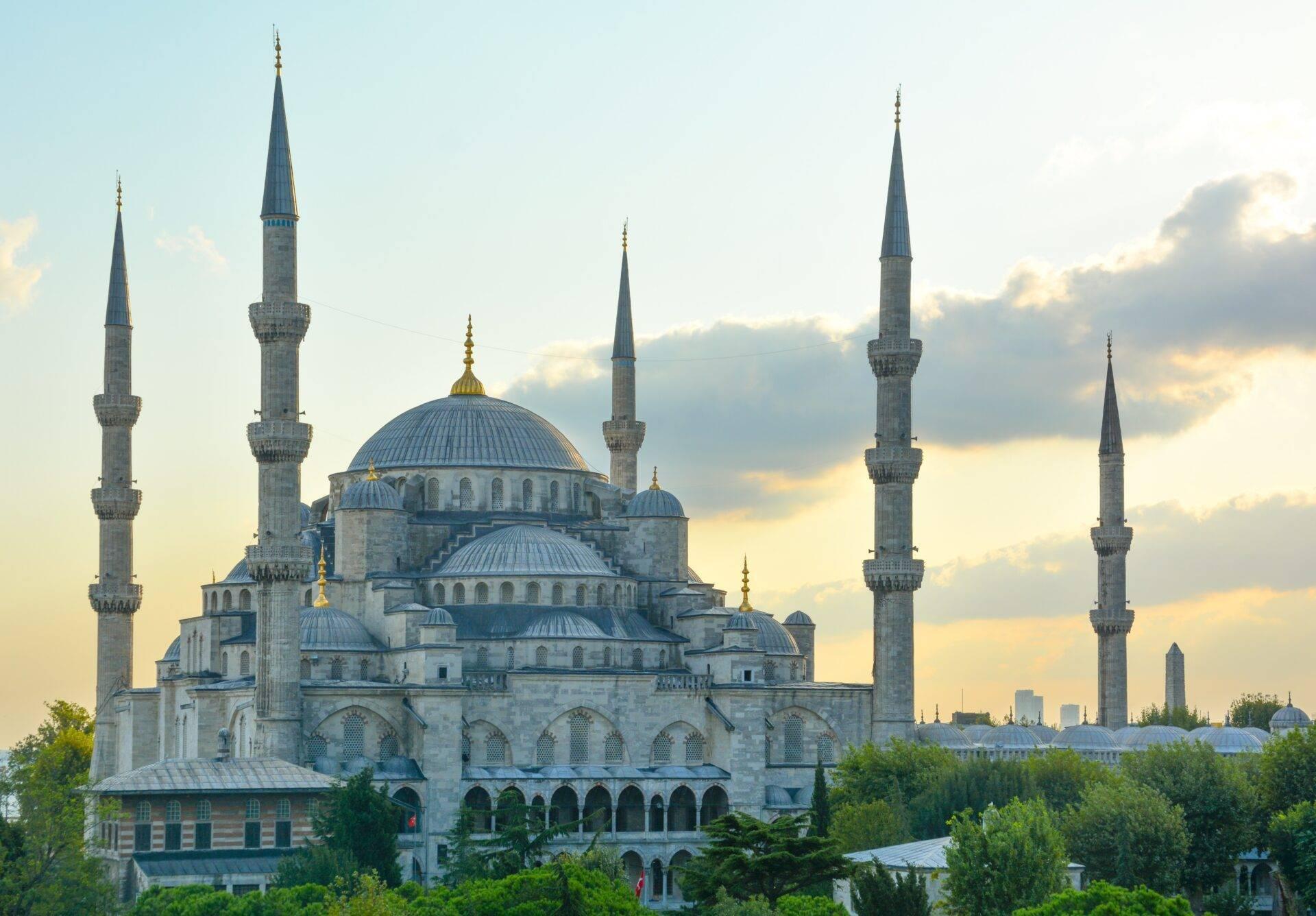 Grande moschea ottomana con sei minareti e cupole dorate, circondata dal verde sotto un cielo nuvoloso