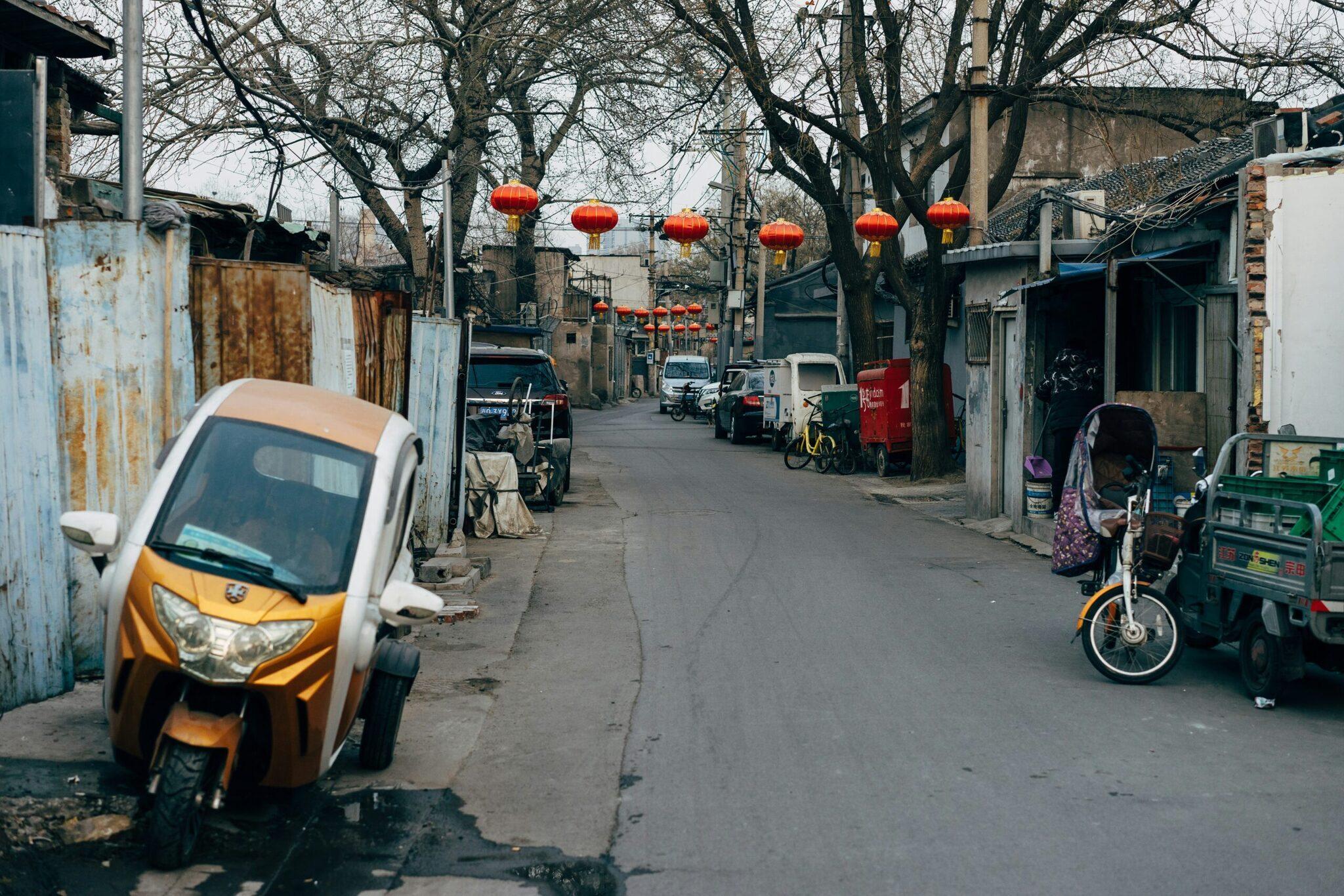 Callejón urbano chino con faroles rojos, vehículos aparcados y edificios residenciales tradicionales