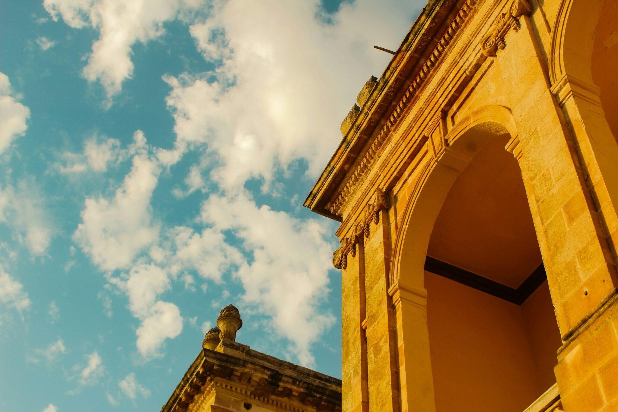 Arc de pierre jaune d’un édifice historique sous ciel bleu avec nuages blancs