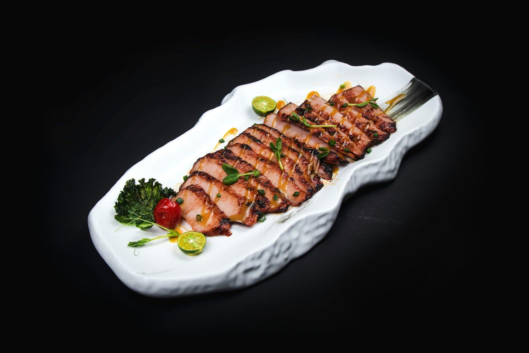 Pato laqueado cortado en lonchas finas presentado en plato blanco con guarniciones frescas, especialidad culinaria asiática