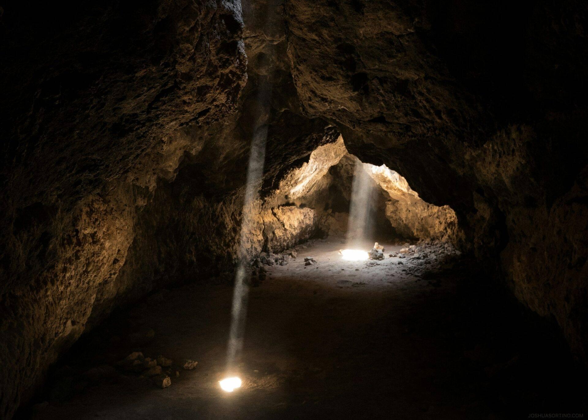 Interior de una cueva calcárea con rayos de luz atravesando la oscuridad y vista de la entrada iluminada