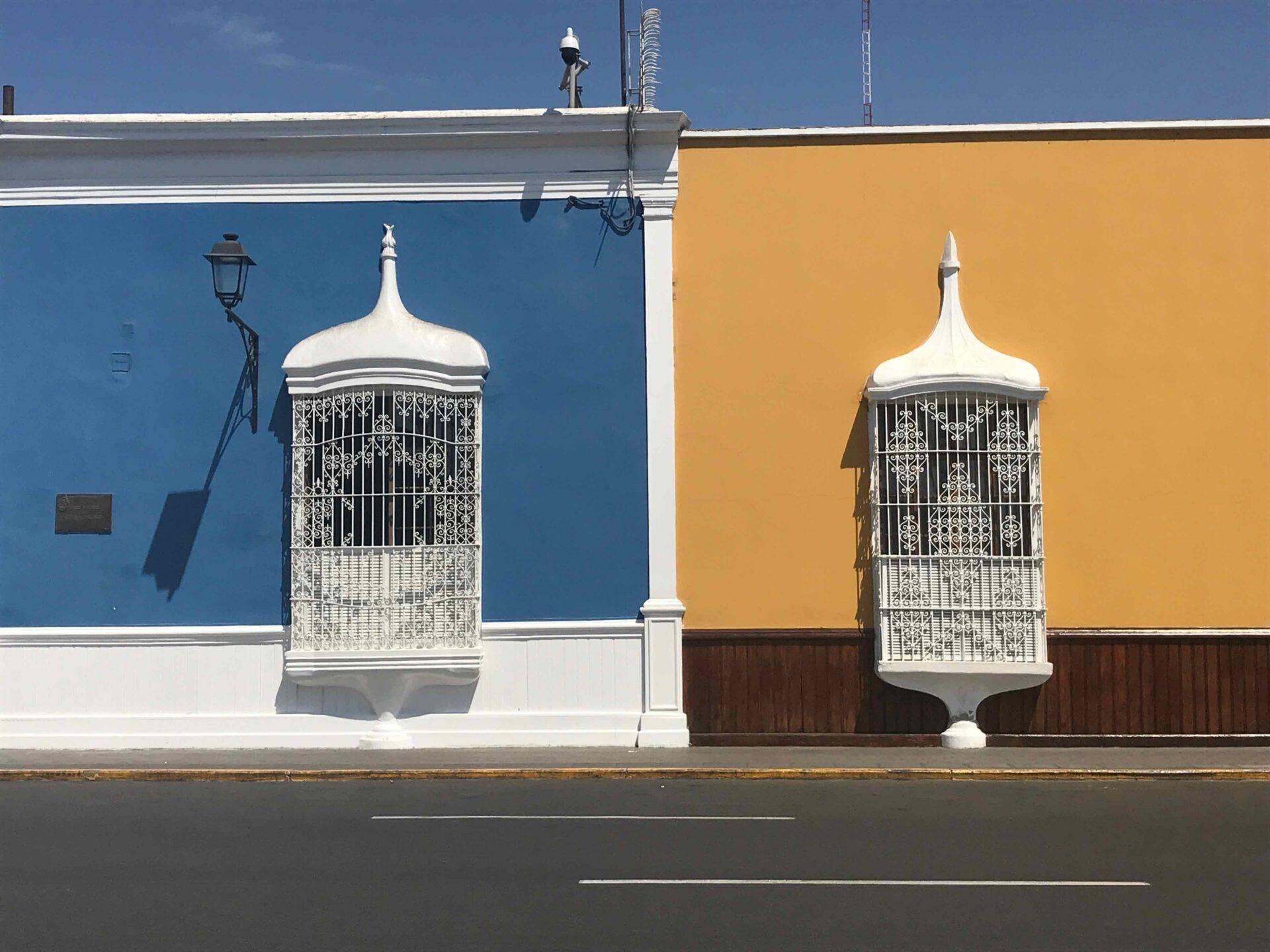 Dos jaulas de pájaros ornamentales blancas sobre fachadas coloniales azul y amarillo de un edificio colonial