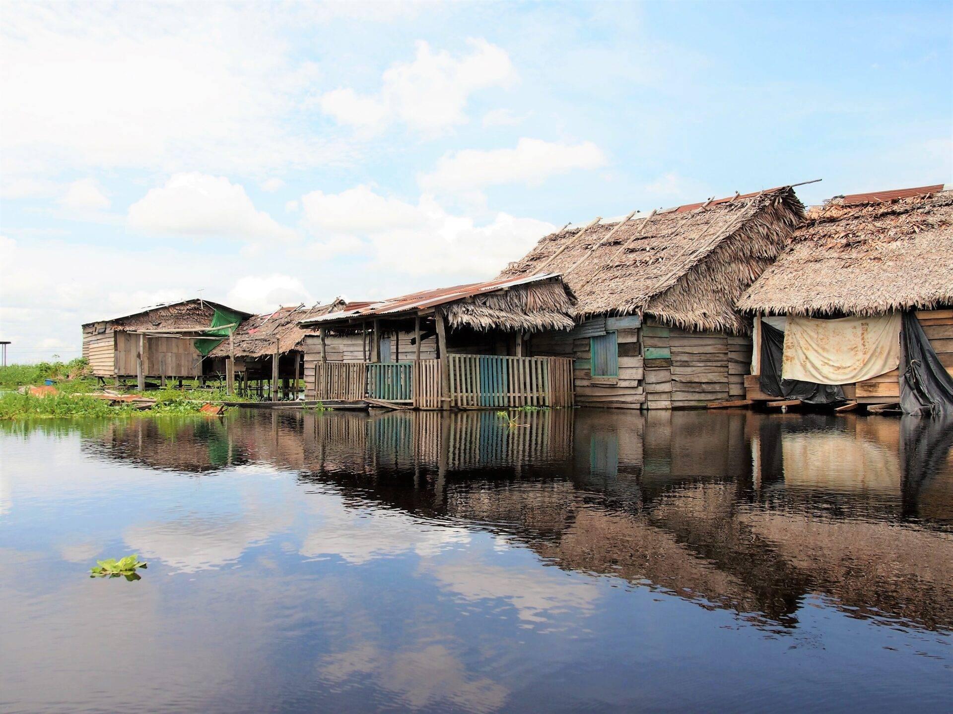 Viviendas sobre pilotes con techos de paja bordean un canal de agua tranquila en la Amazonía