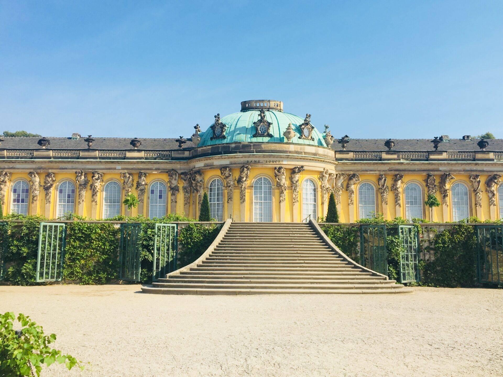 Un palazzo barocco giallo ornato da una cupola verde turchese con una scalinata monumentale in pietra