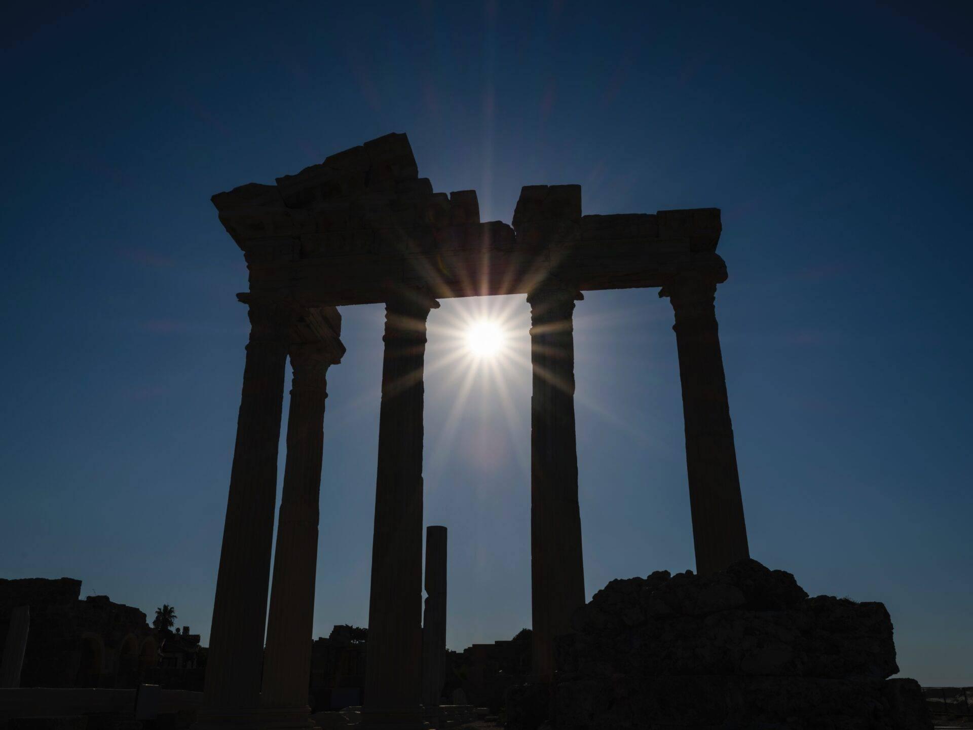 Silhouette di colonne antiche controluce sotto un cielo blu sgombro