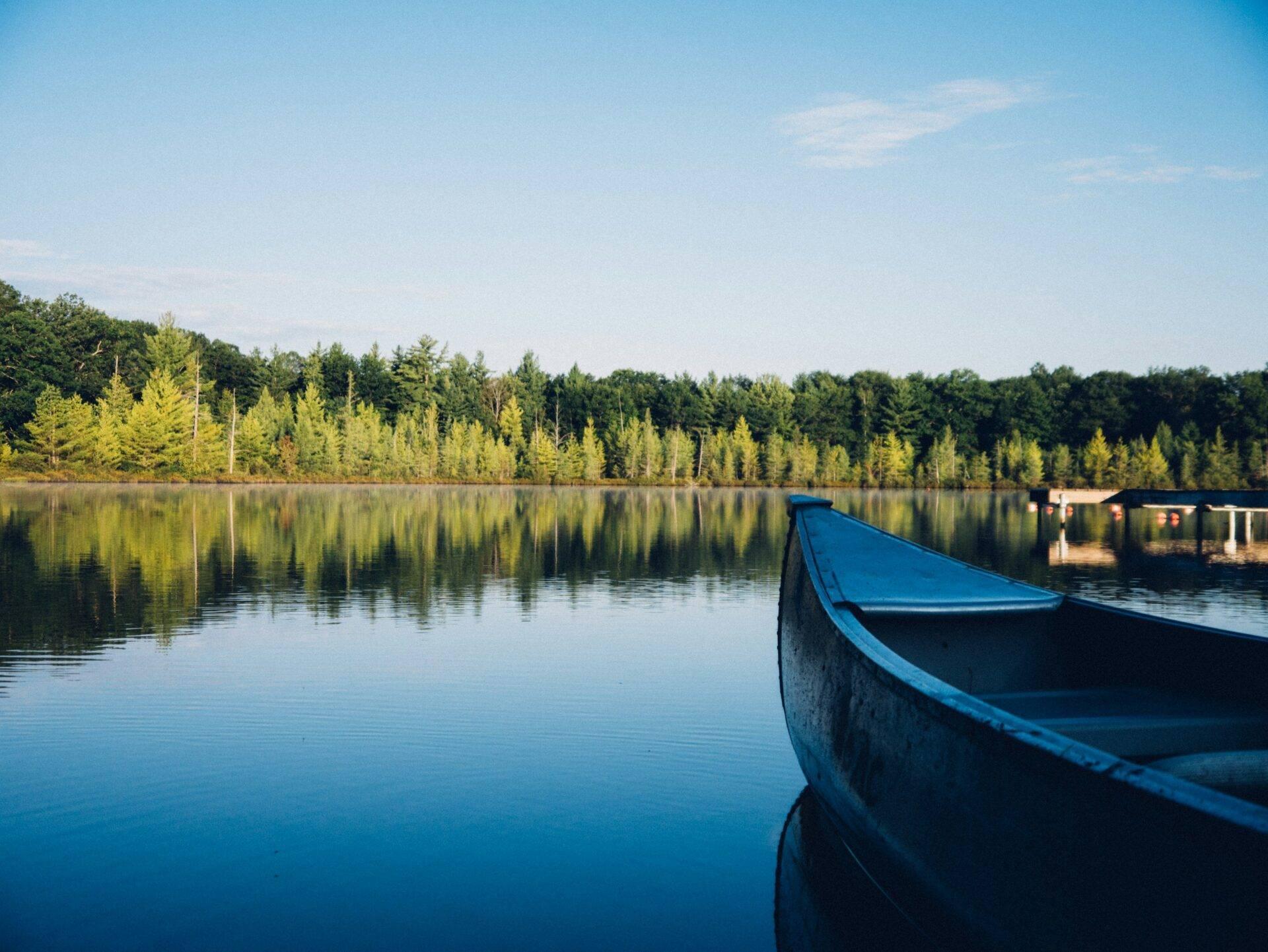 Un barco azul amarrado en un lago tranquilo bordeado de bosques de coníferas bajo un cielo despejado