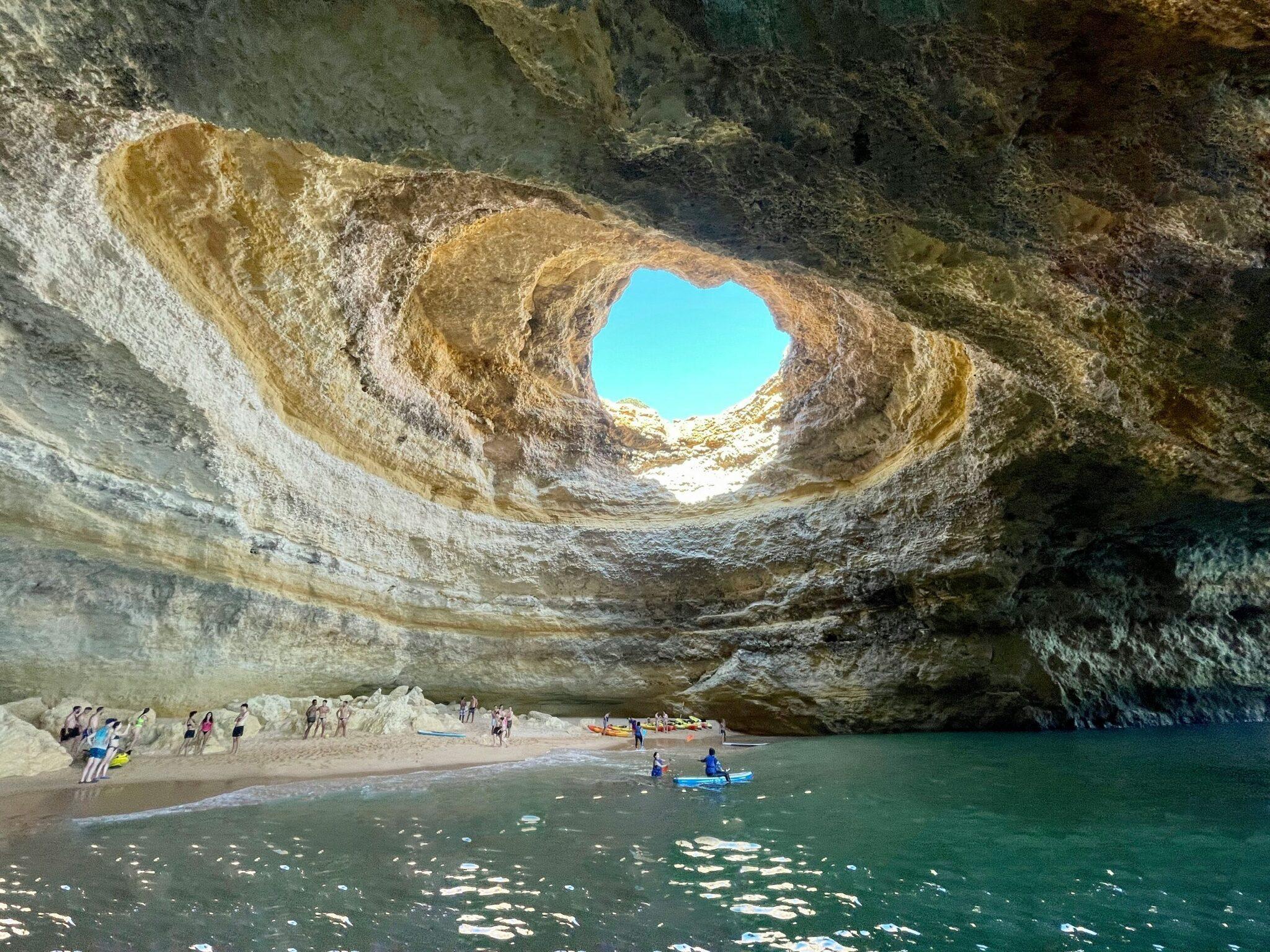Ein verborgener Strand unter einer riesigen Kalksteinhöhle mit einem kreisrunden Loch in der Decke, durch das natürliches Licht einfällt