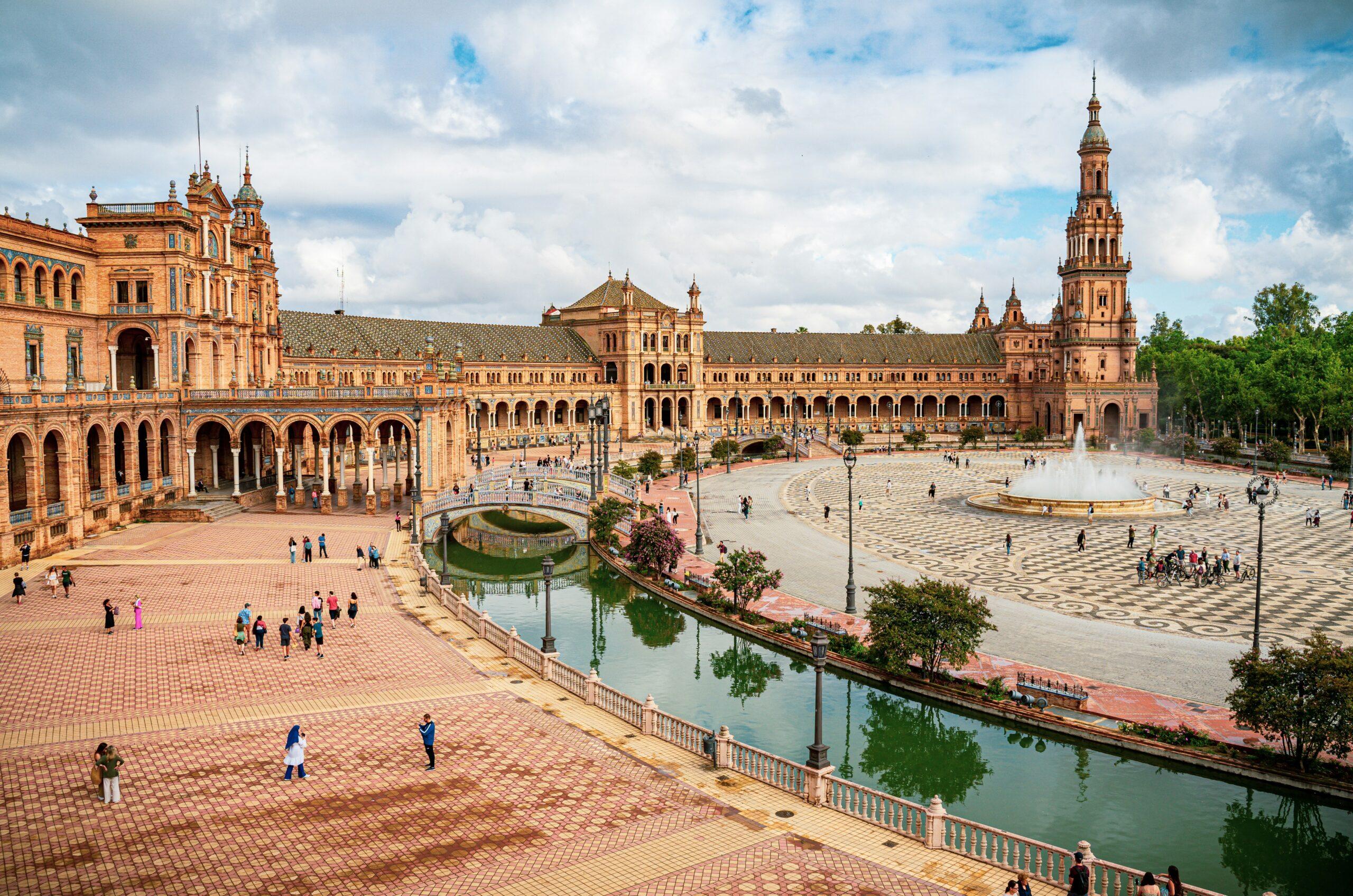 Gran plaza con edificios de ladrillo ocre, canal y fuente bajo un cielo nublado